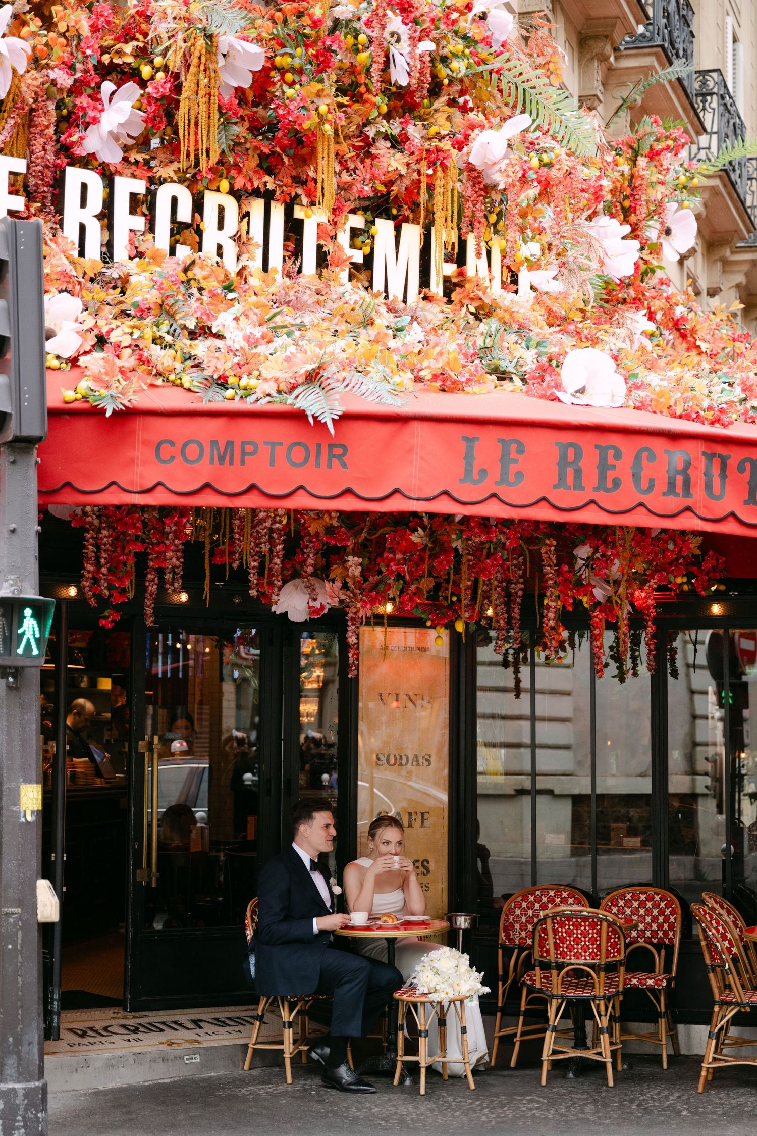 French cafe terrace with pink floral decorations and red awning displaying 'Le Recrutement' signage.