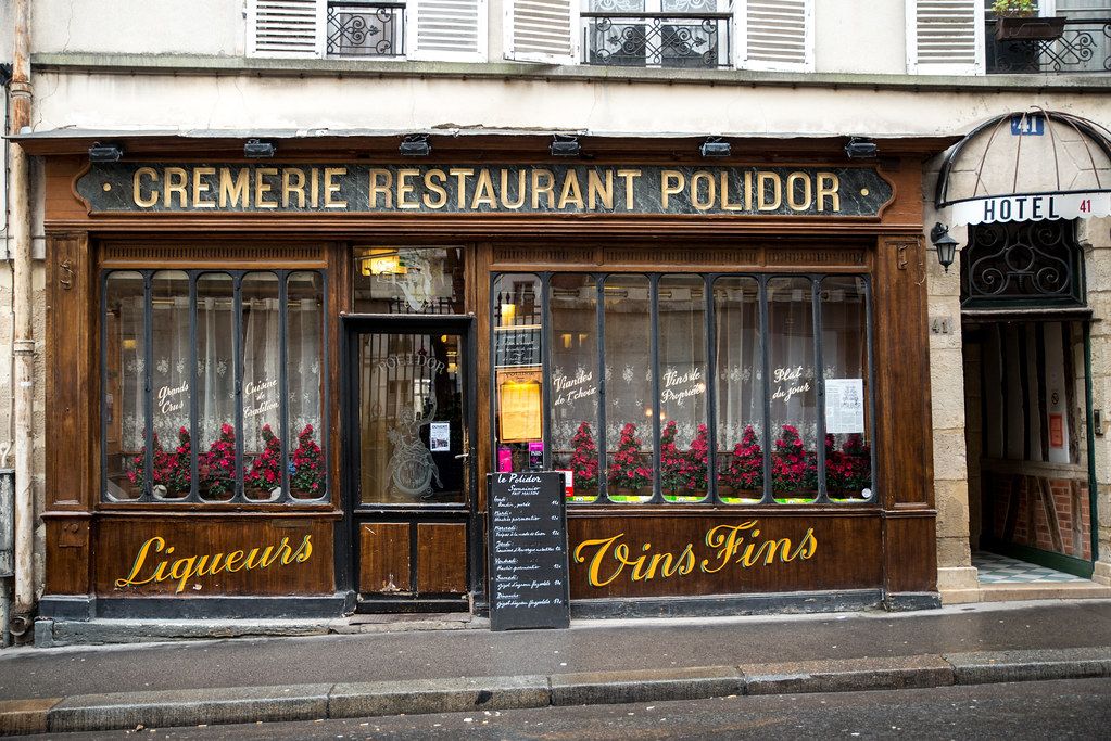 Traditional French restaurant storefront with vintage wood facade and signage for liqueurs and wines.