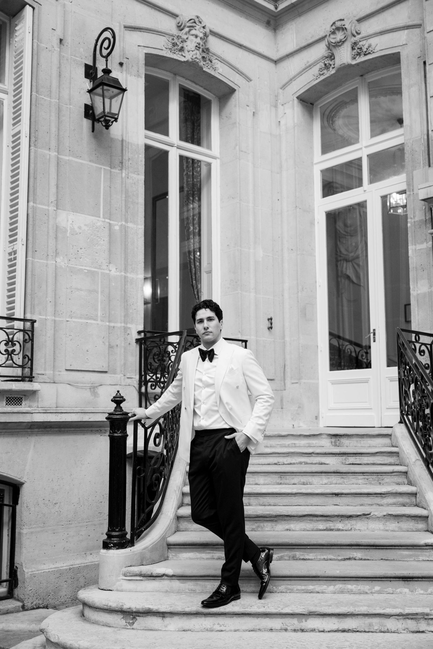 Dapper groom in white tuxedo poses on stone steps of a classic Parisian building.