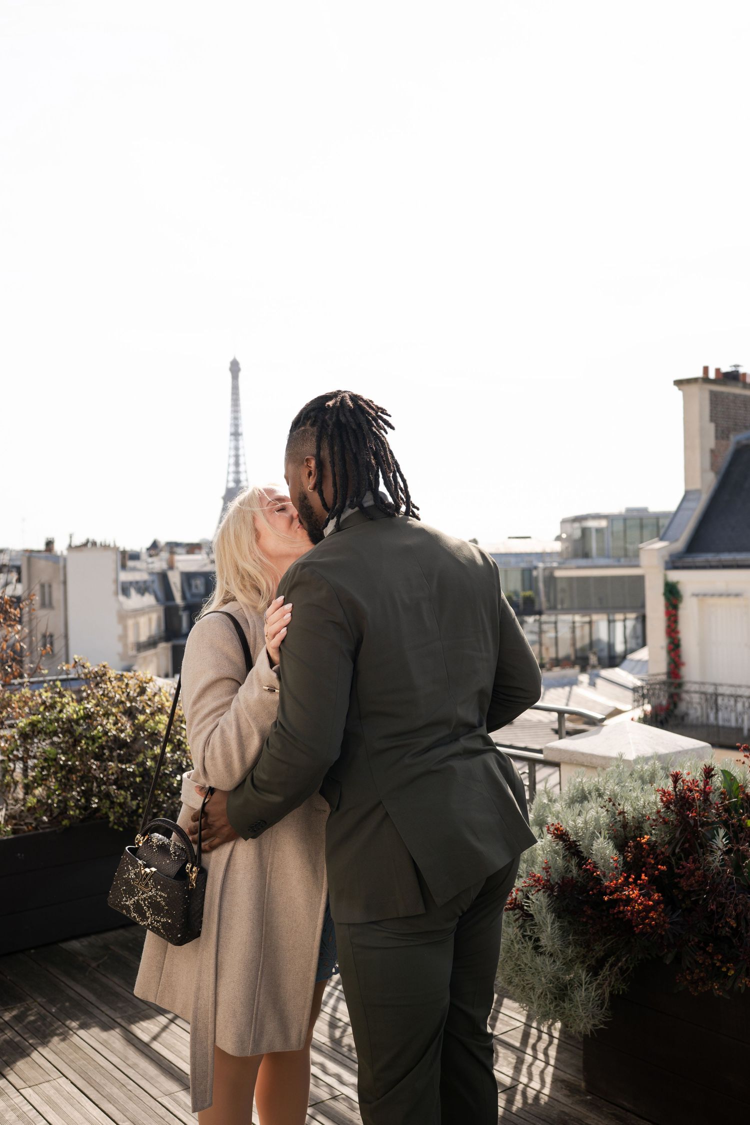 Couple kissing on a Parisian rooftop terrace with the Eiffel Tower visible in the background.