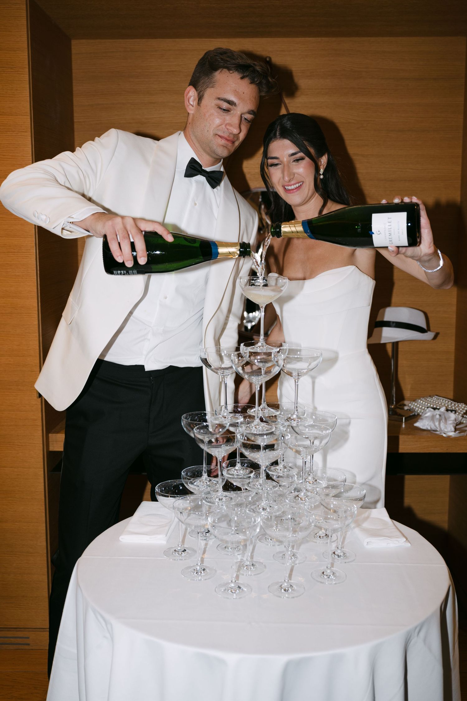 Bride and groom pouring champagne over a crystal glass tower at their wedding reception.
