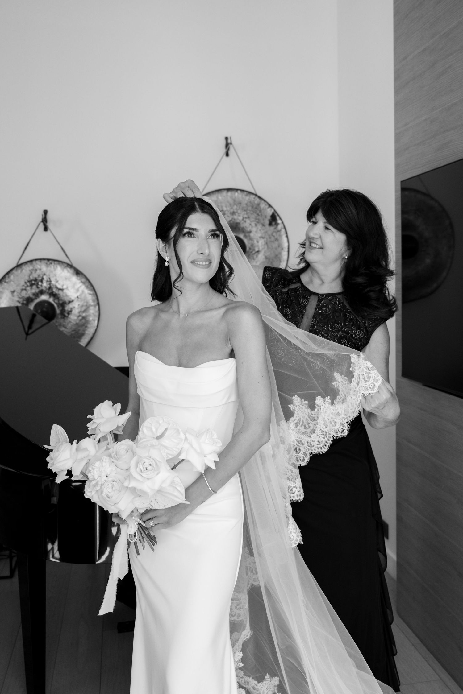 Black and white photo of mother adjusting bride's lace veil before Paris wedding ceremony indoors.