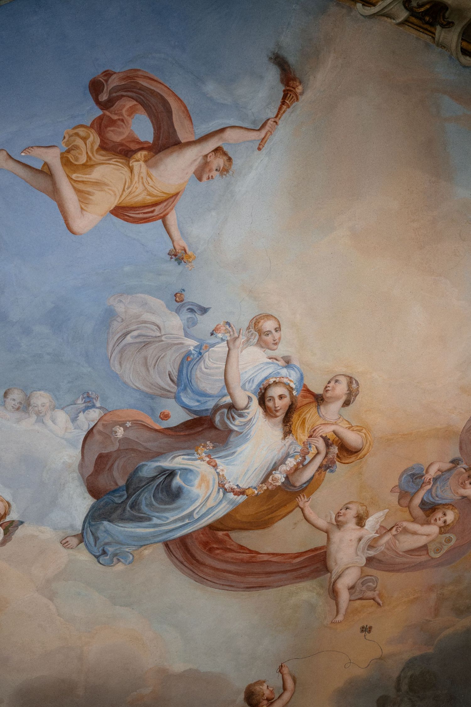 Baroque ceiling fresco depicting elegant figures floating among clouds with cherubs and torch bearer.