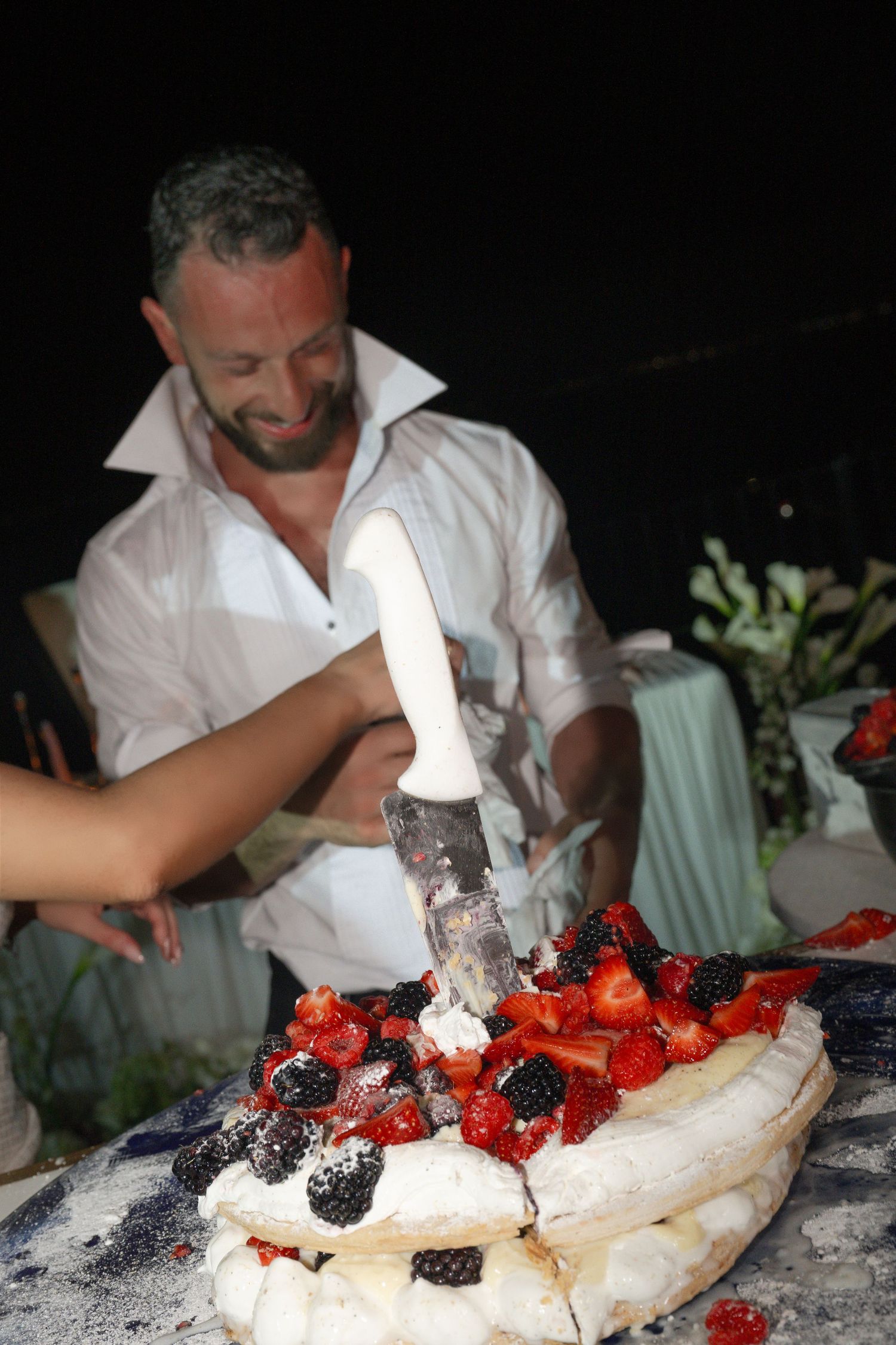 Groom cutting berry-topped wedding cake with knife at reception.