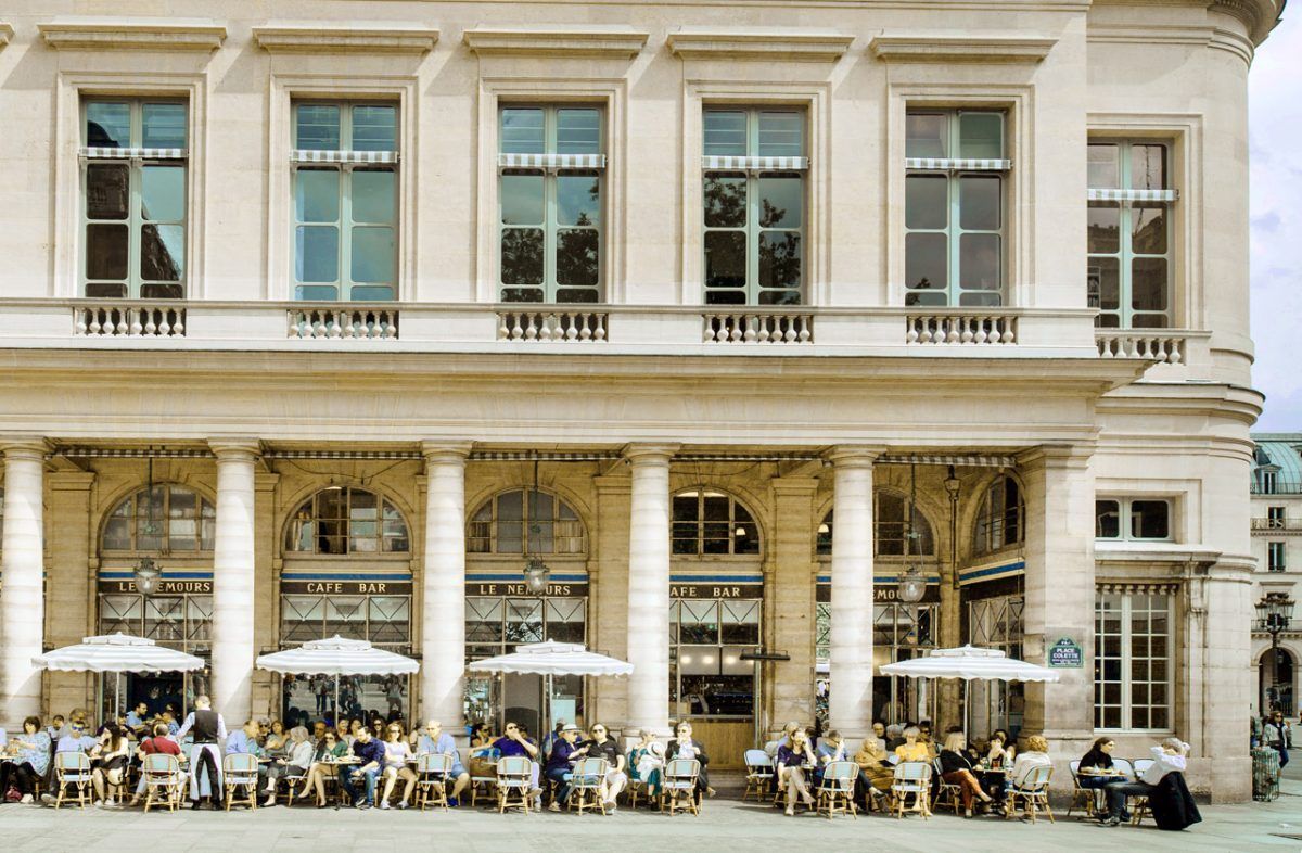 Classic Parisian cafe terrace with outdoor seating and elegant cream-colored architecture.