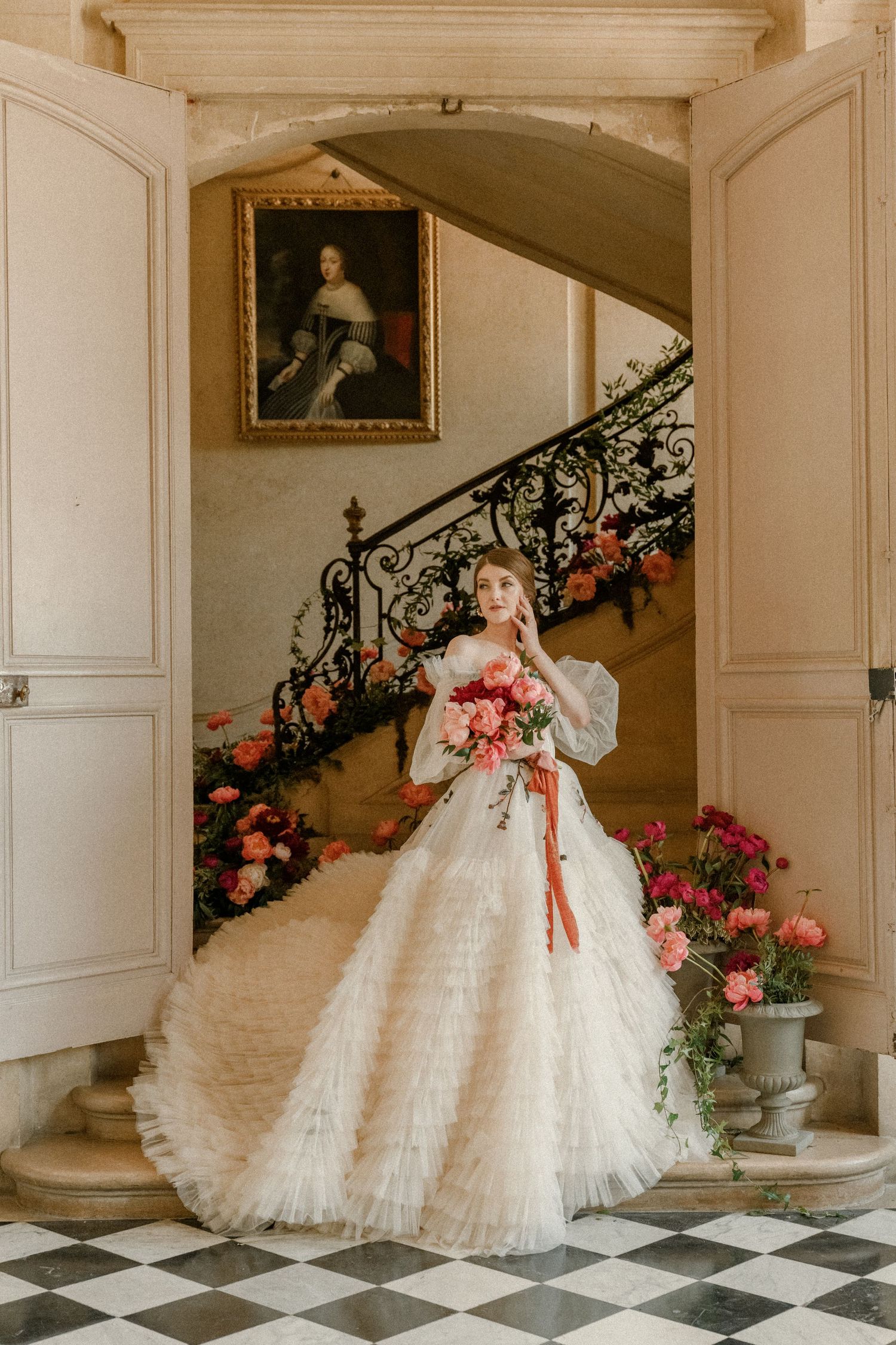 Elegant bridal portrait in a grand foyer with checkerboard floor and ornate staircase.