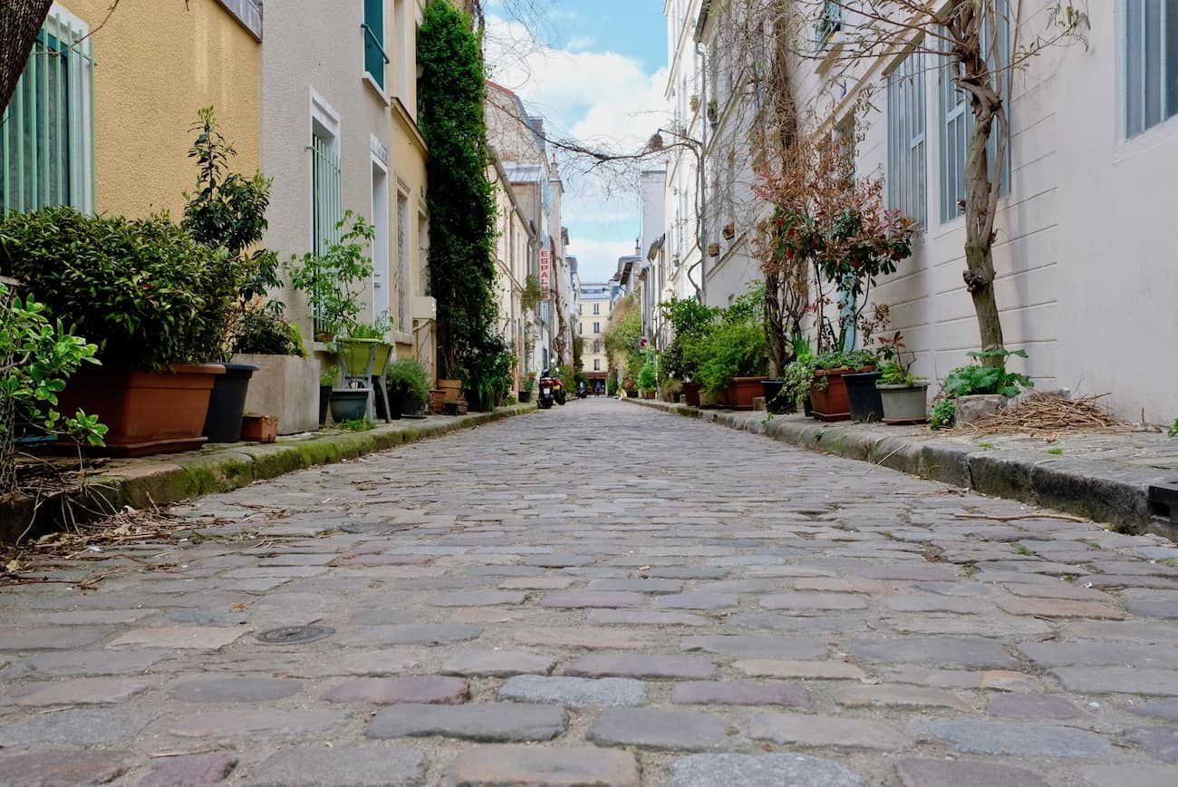 Quaint cobblestone street lined with colorful buildings and potted plants in a European neighborhood.