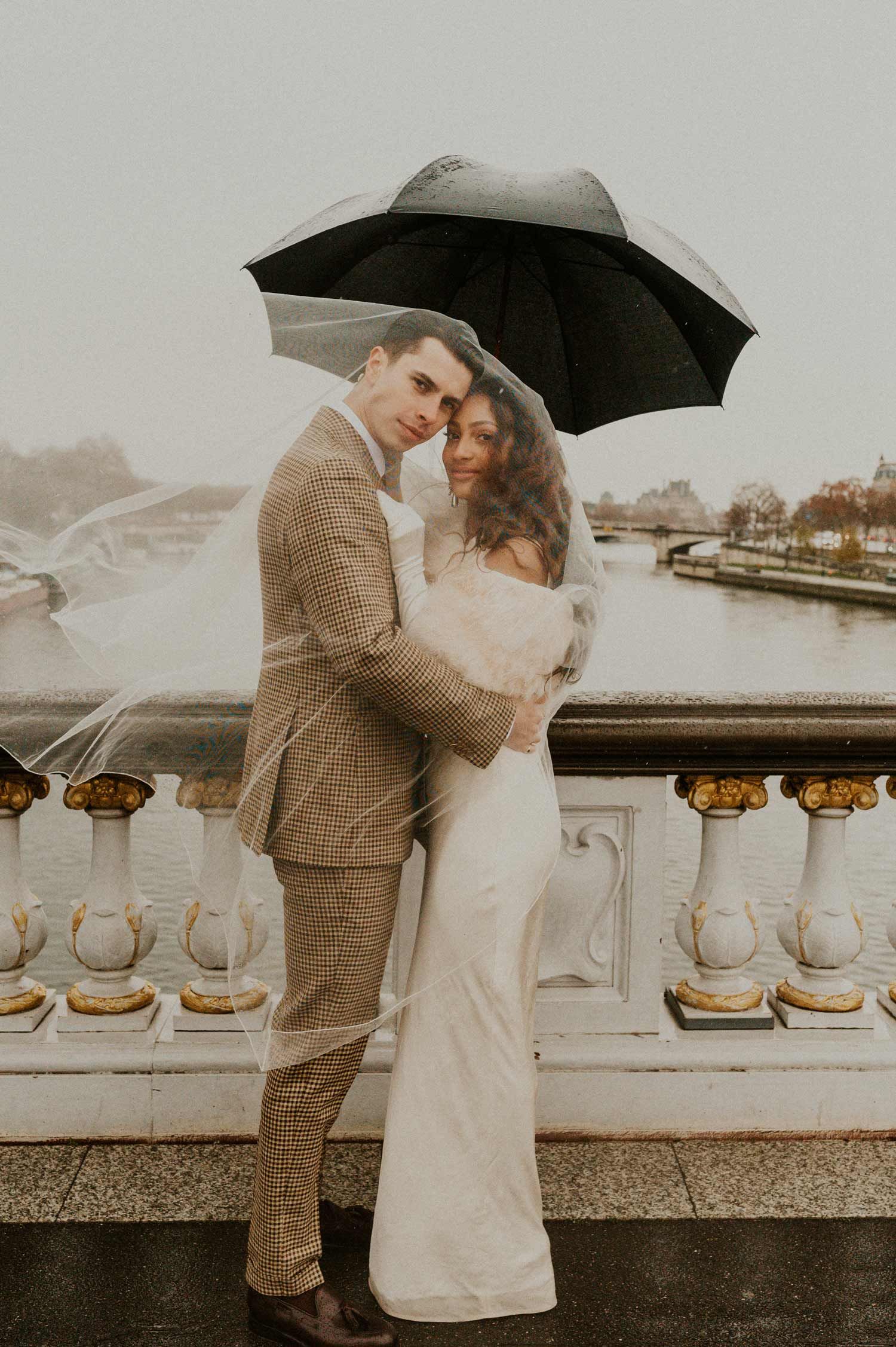 A tender embrace between a couple in formal attire standing by an ornate stone balustrade.