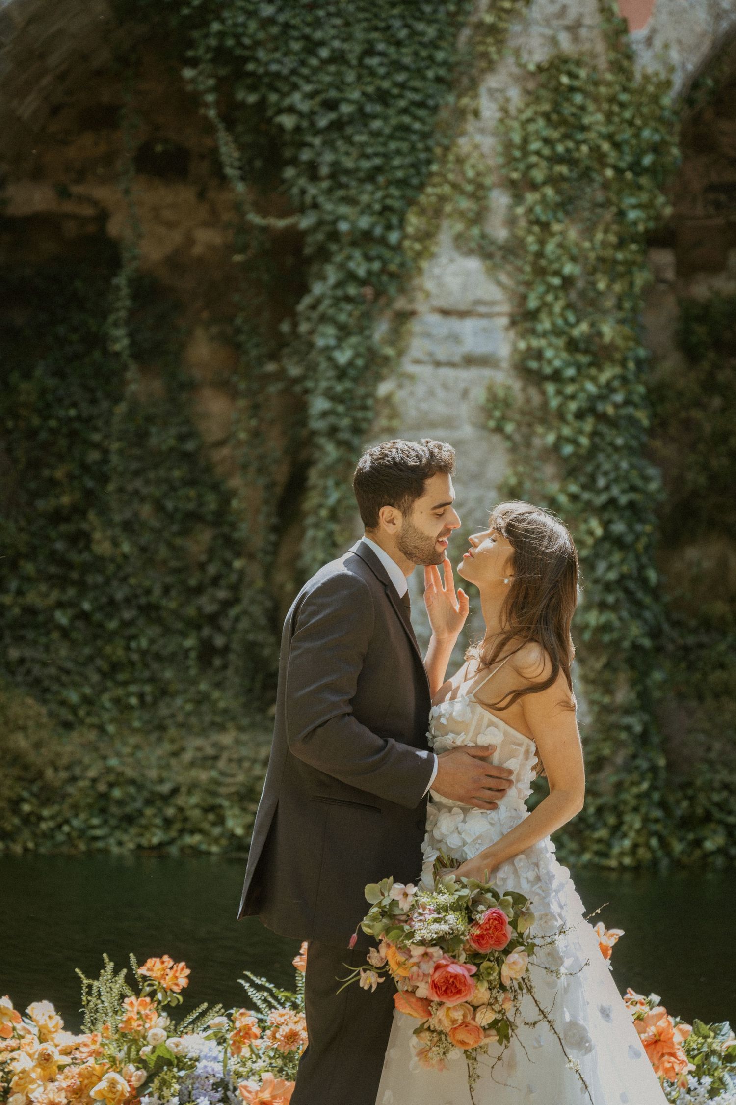 Bride and groom share a romantic moment surrounded by ivy-covered walls and colorful floral arrangements.