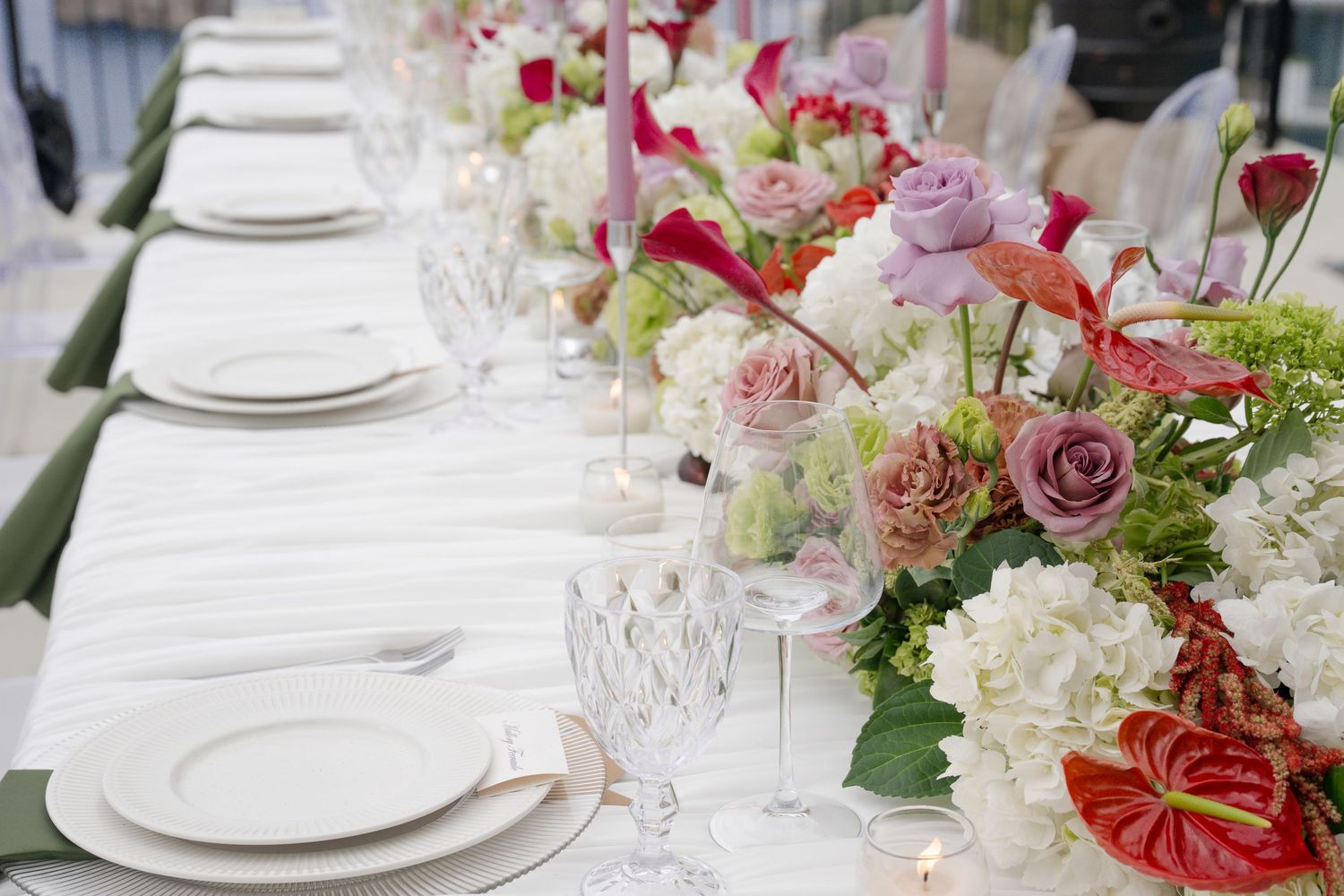 Elegant wedding tablescape with white linens, crystal glassware, and colorful floral centerpieces including roses and anthuriums.