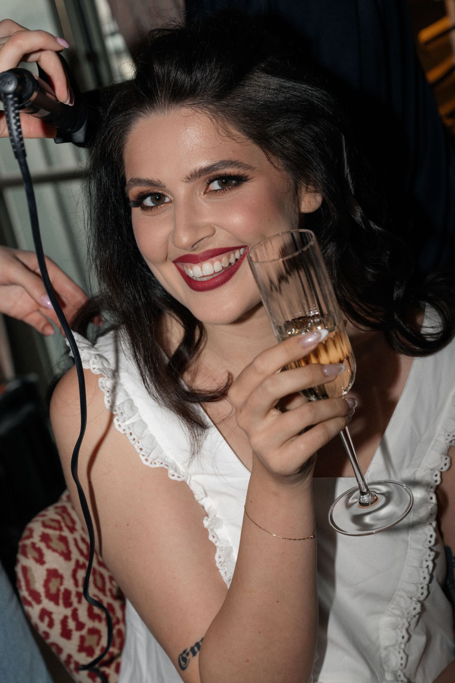 Smiling brunette woman in white dress holding champagne flute at a party.
