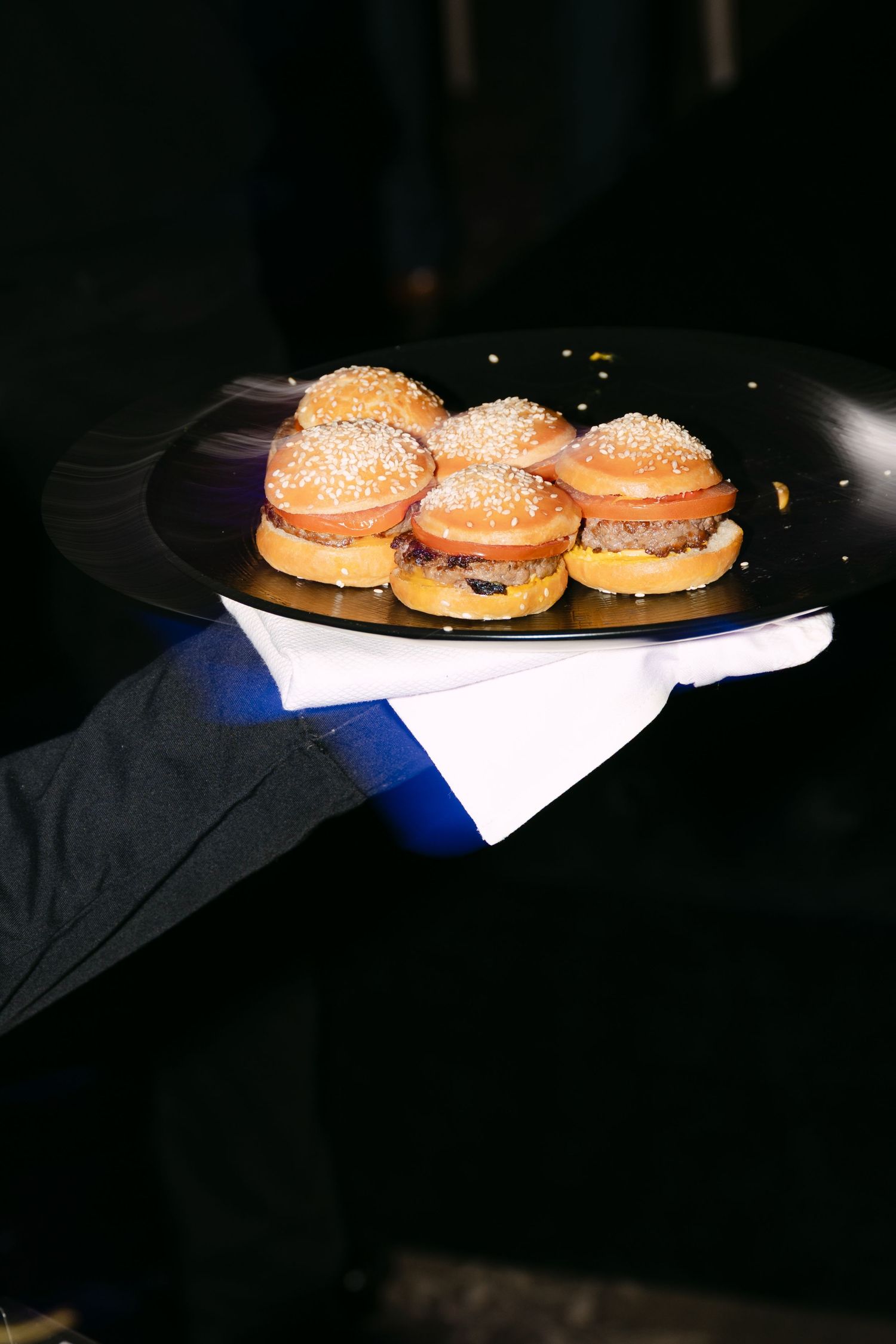 Waiter serving mini cheeseburger sliders on a black plate at an upscale catered event.