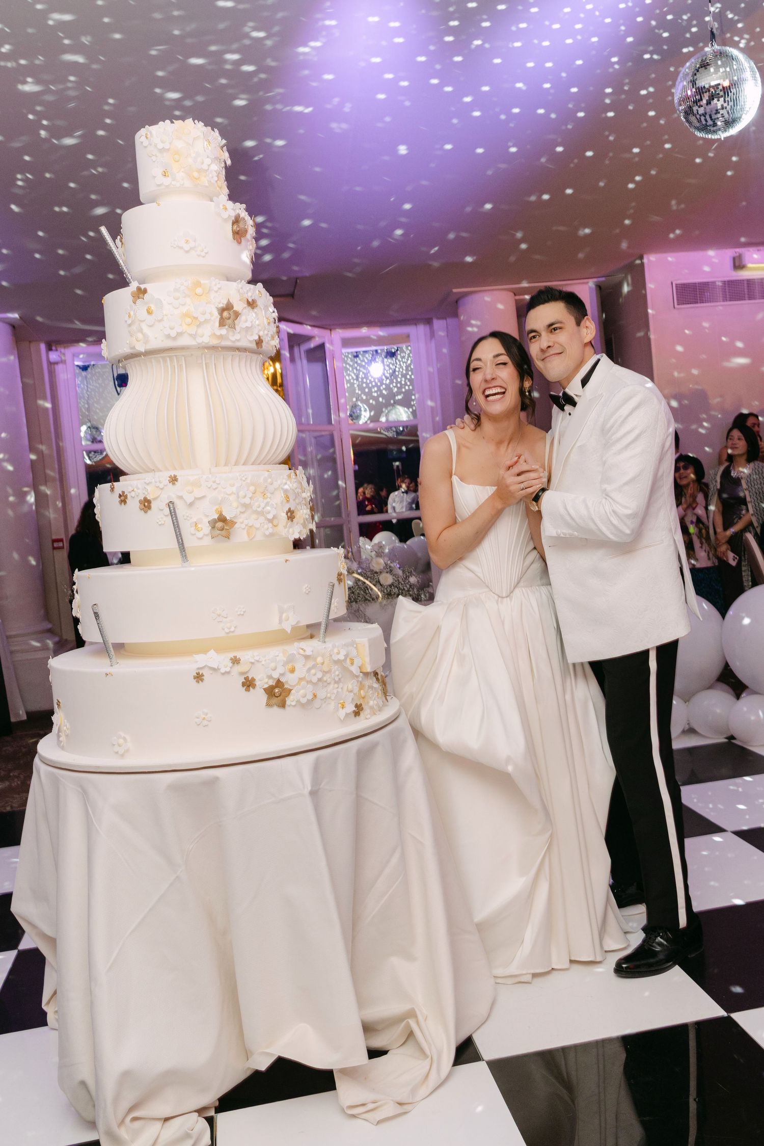 Smiling bride and groom standing beside tall white gold-star wedding cake on dance floor.
