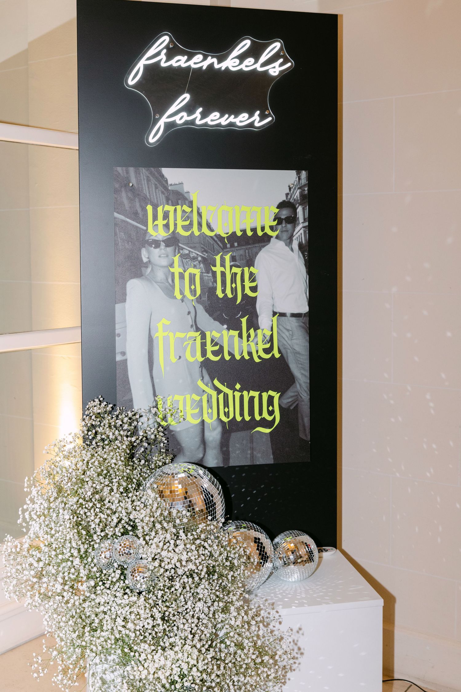 Fraenkels Forever wedding welcome sign with neon lights, baby's breath flowers and disco balls.
