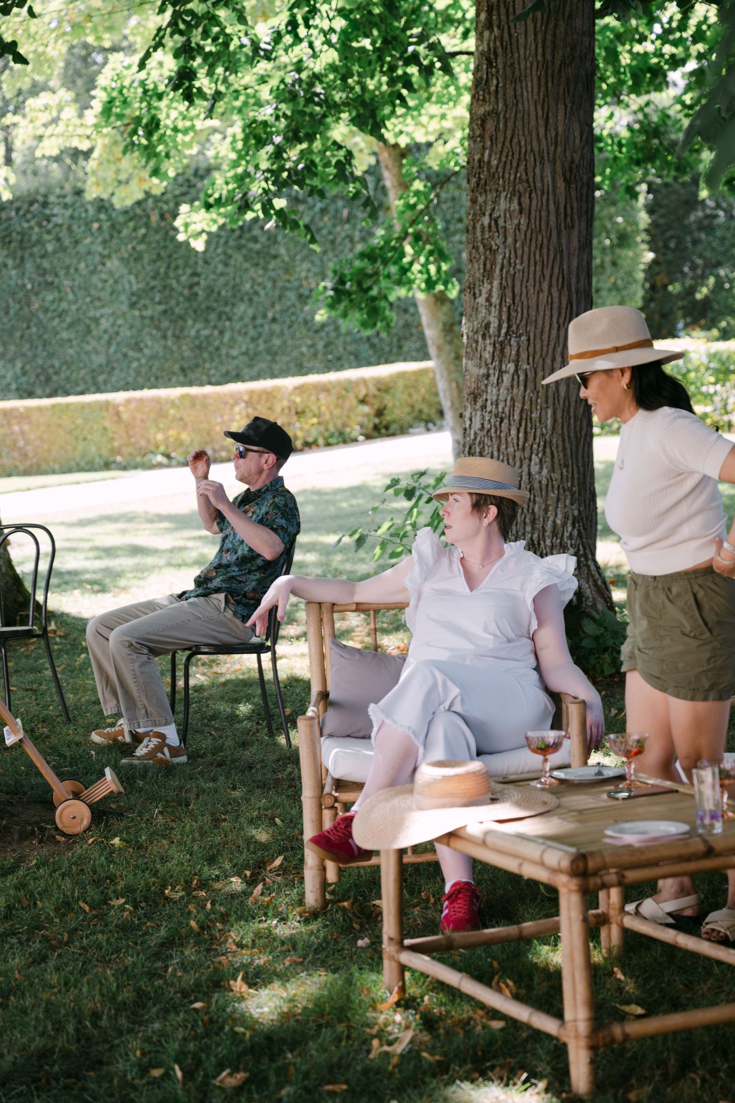 Wedding guests relaxing on bamboo chairs under a large tree at an elegant outdoor garden reception.