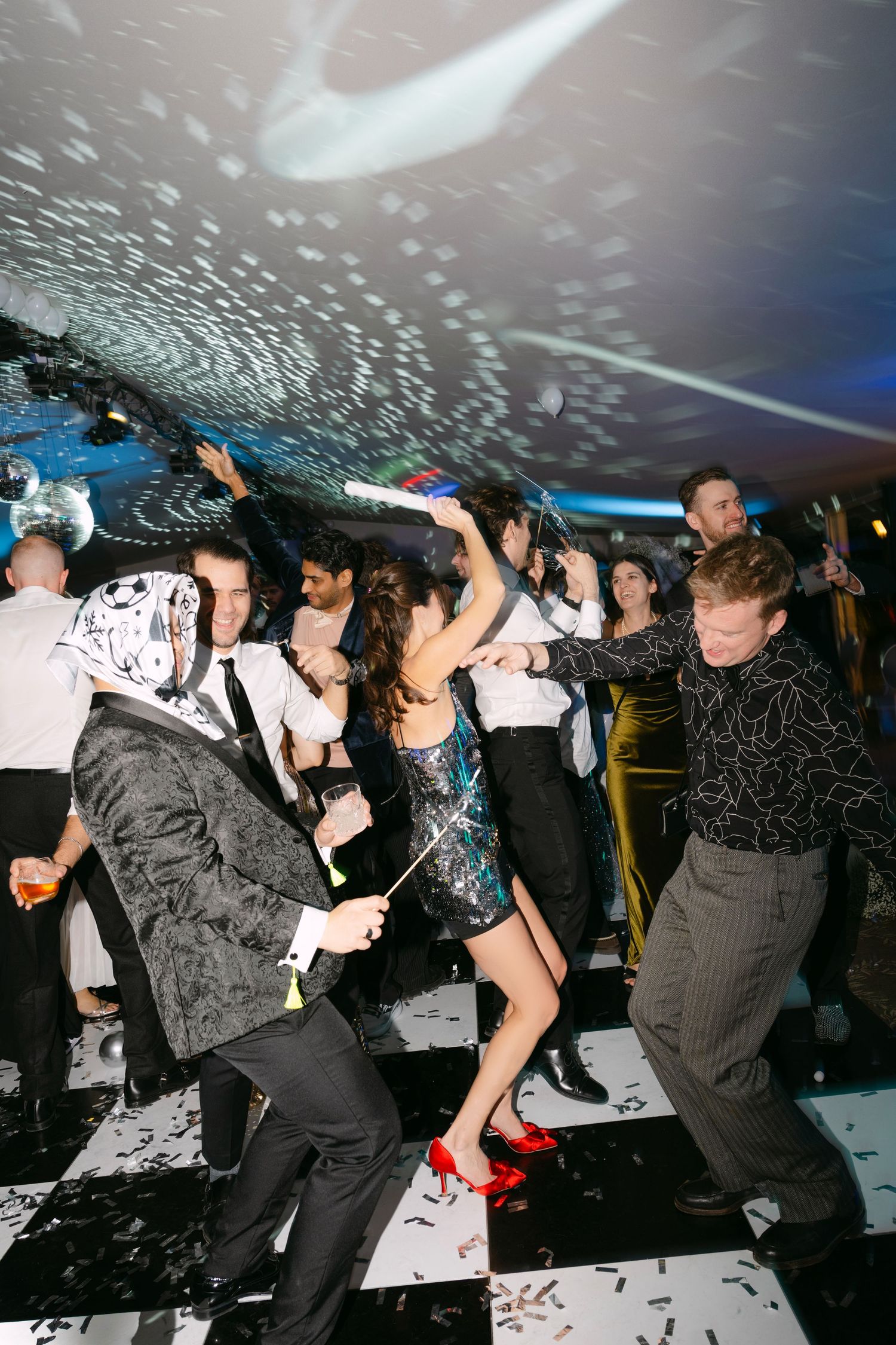 Guests dancing energetically with confetti on black and white dance floor at festive wedding reception.