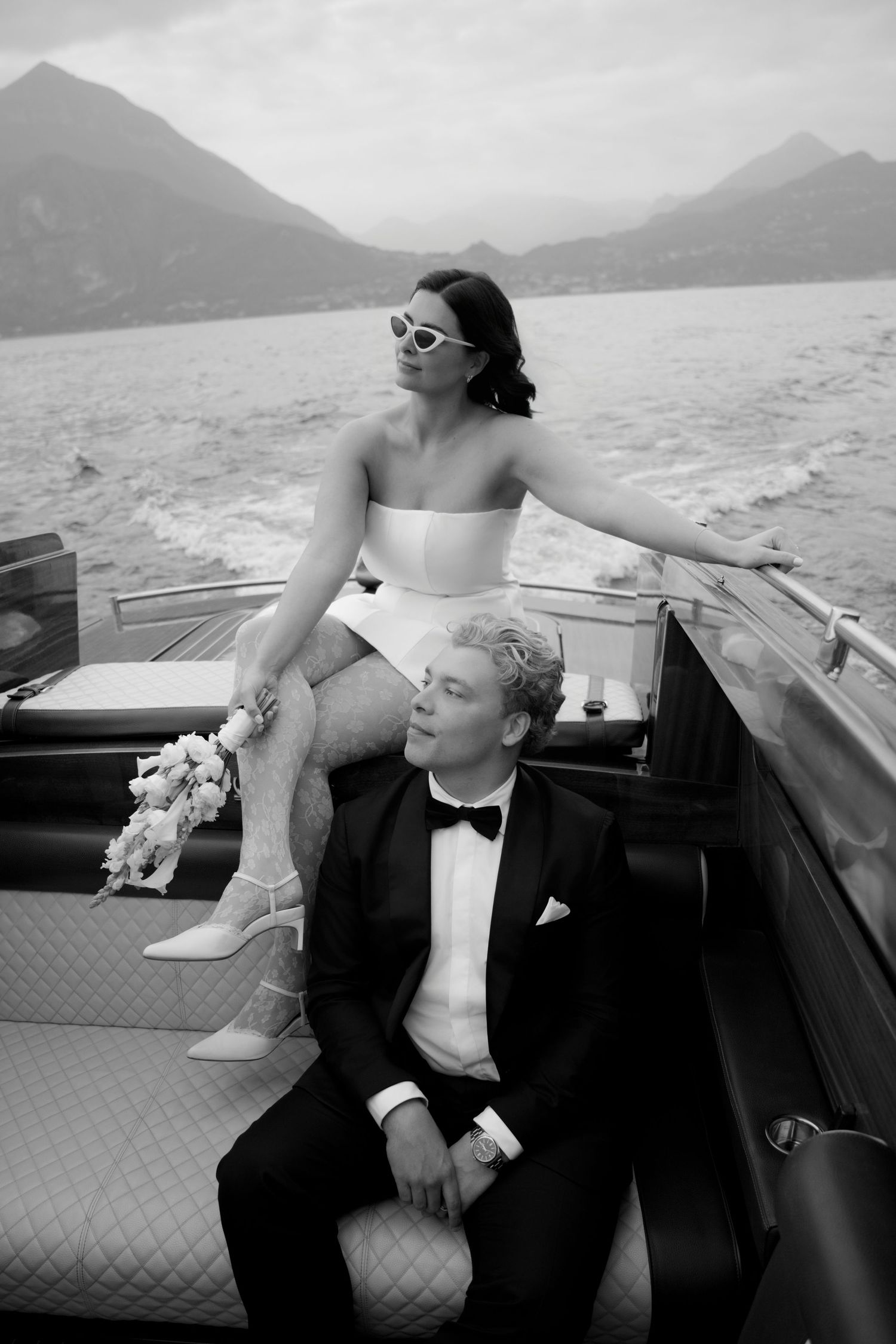 Black and white photo of a bride and groom on a luxury boat with mountain lake backdrop on their wedding day.