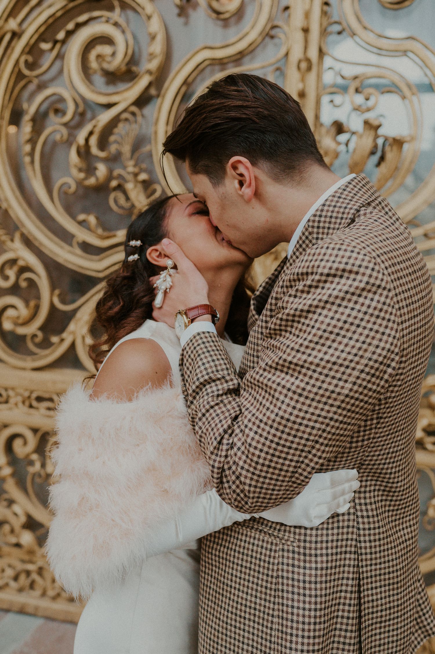 A romantic wedding couple kiss against an ornate gold baroque background wall.