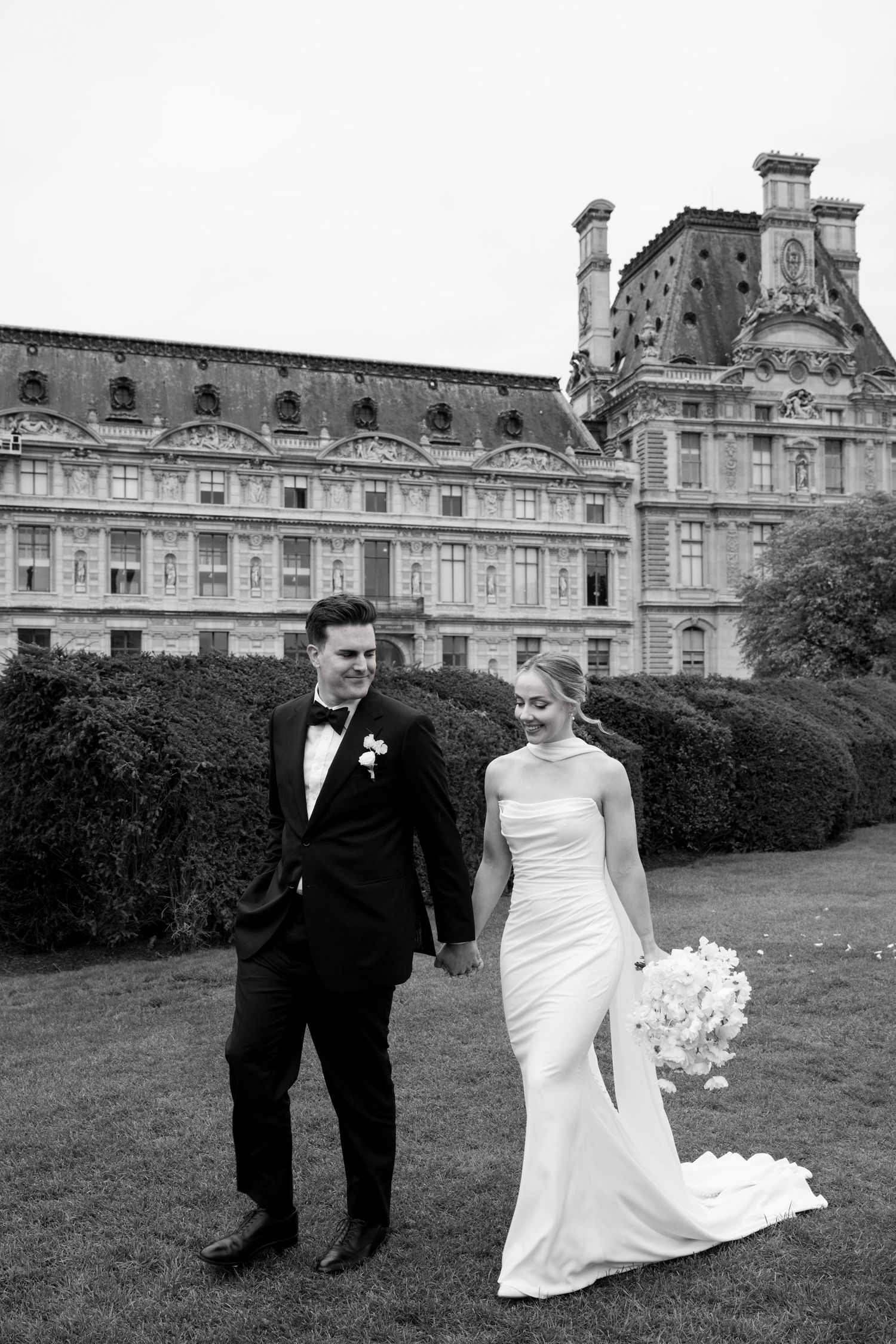 A bride and groom share a moment together on the lawn in front of a grand historic European building.