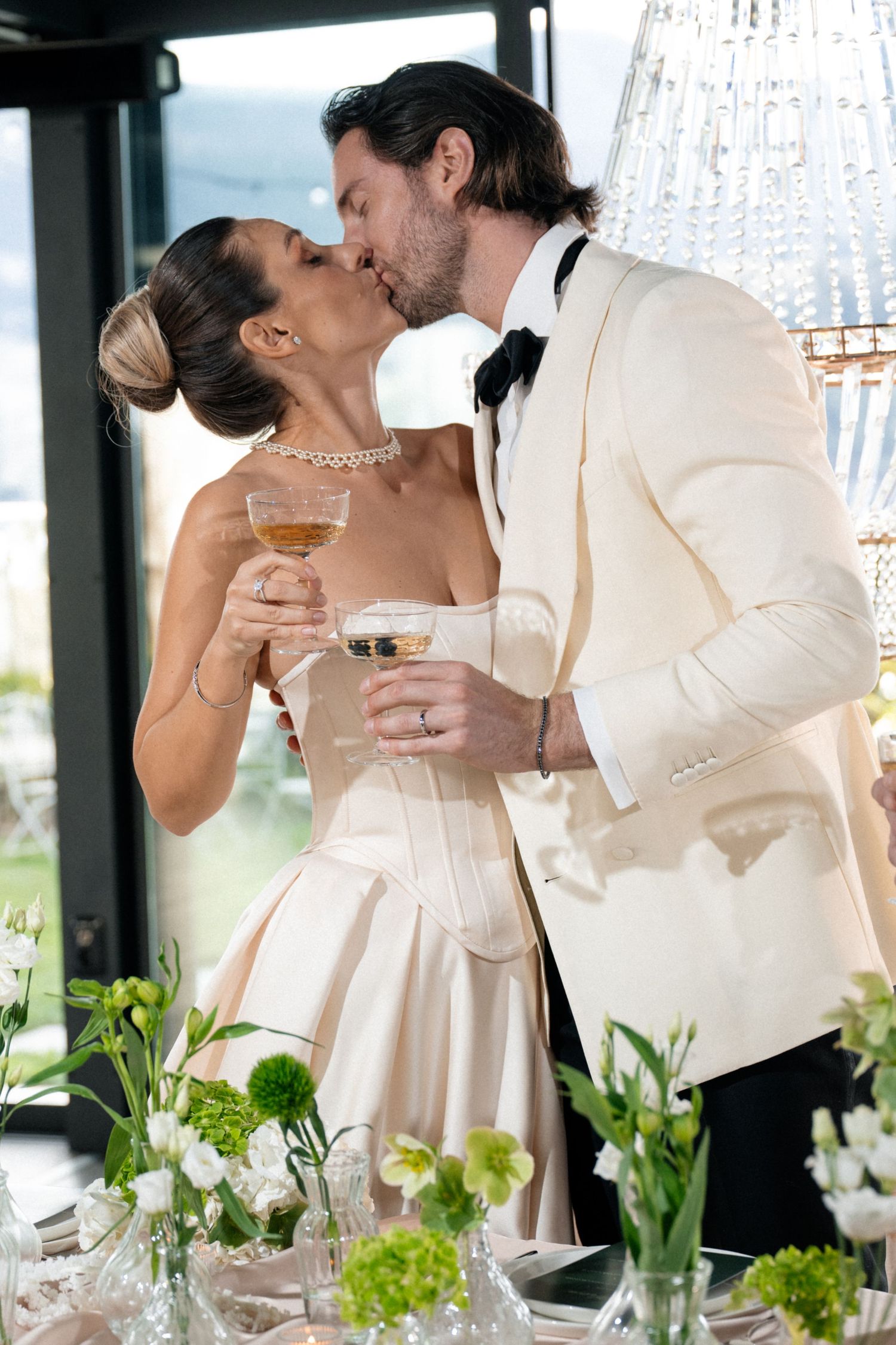 Stylish couple poses under arched colonnade with palm trees visible in background, captured in black and white.