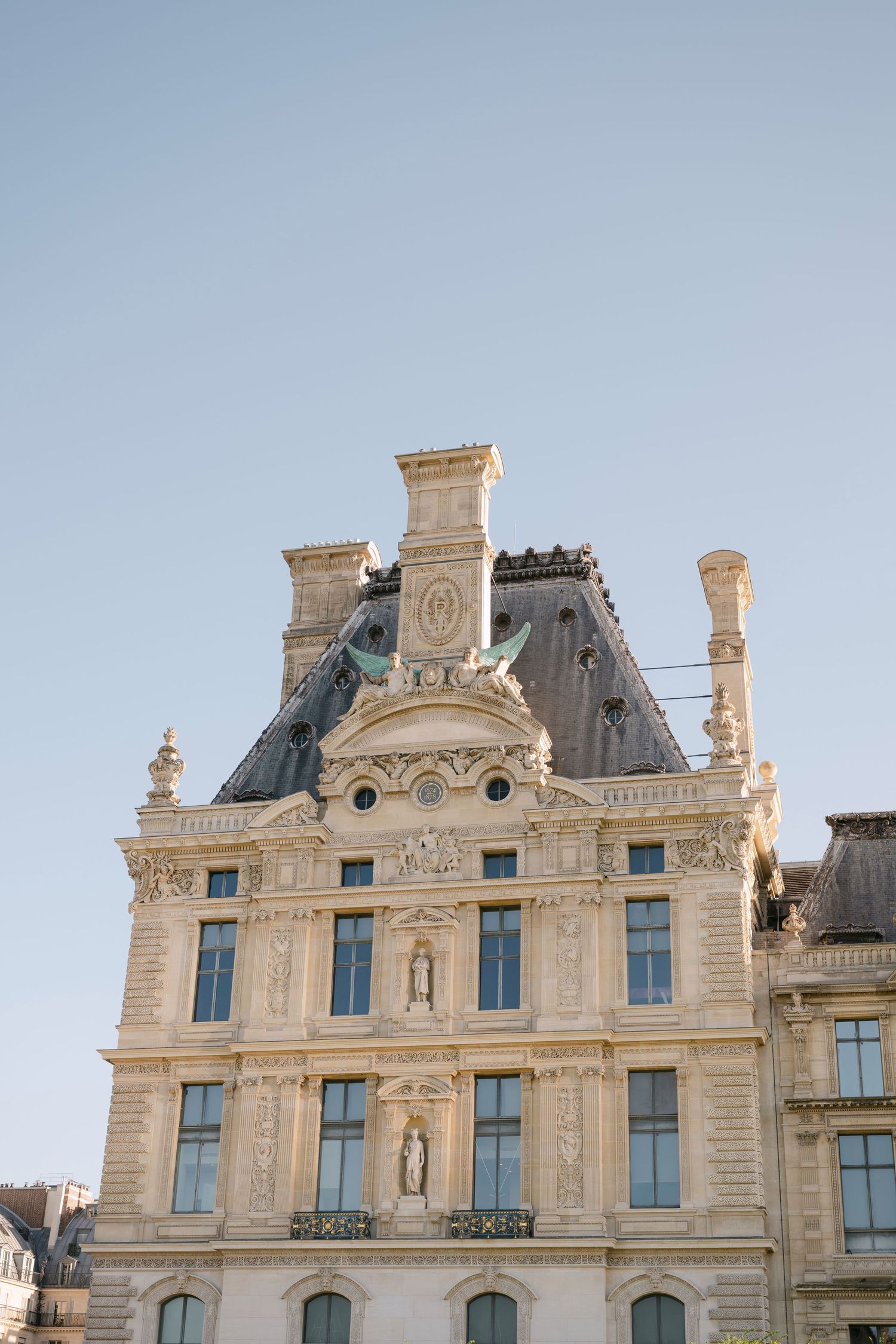 Ornate Haussmann-style Parisian building facade with sculptures against clear blue sky.