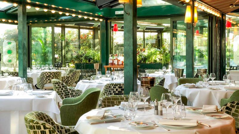 Elegant restaurant interior with white tablecloths, green accent chairs, and ornate patterned details.