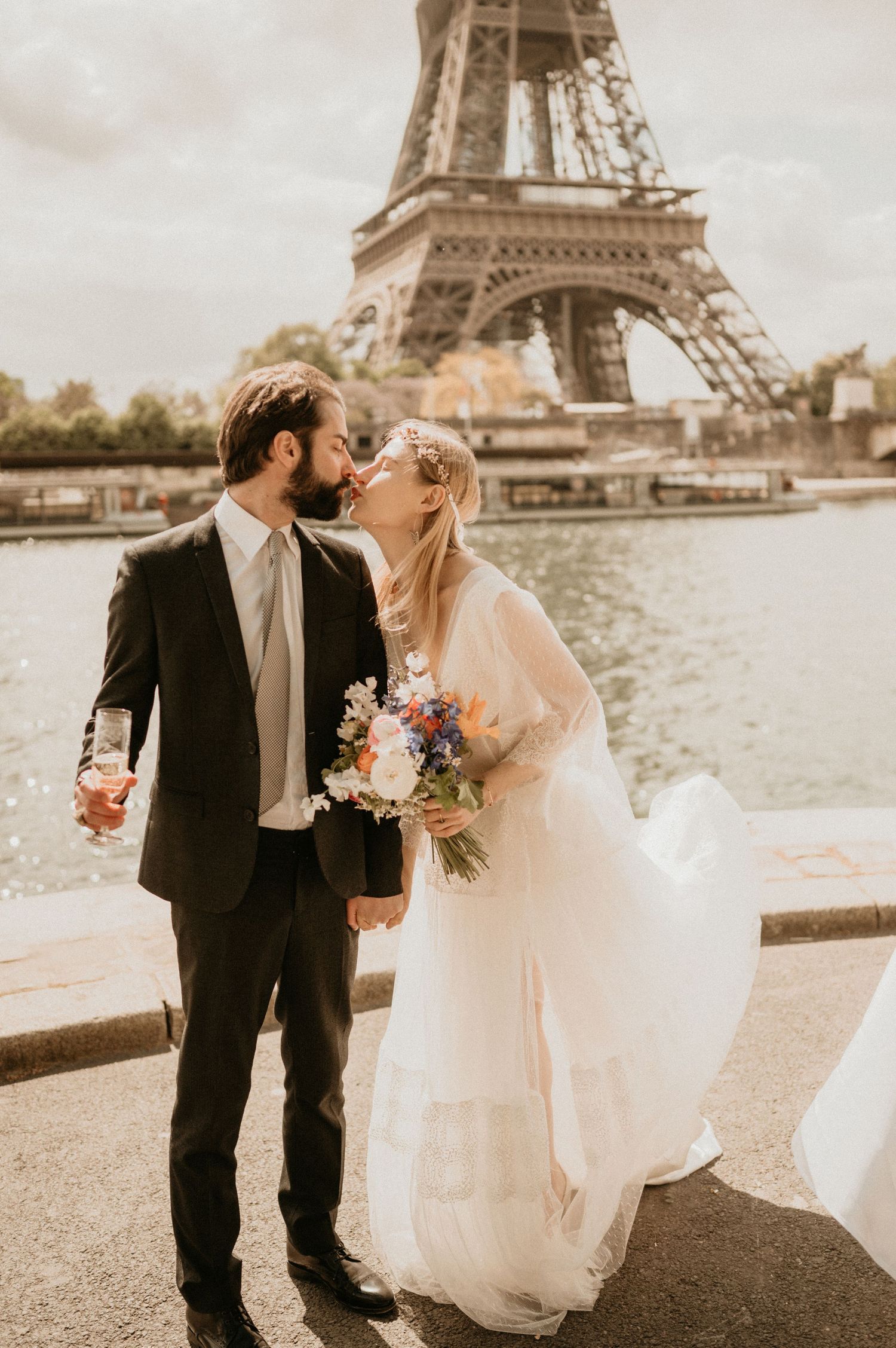 Newlyweds share a romantic moment with flowers in hand near the Eiffel Tower in Paris.