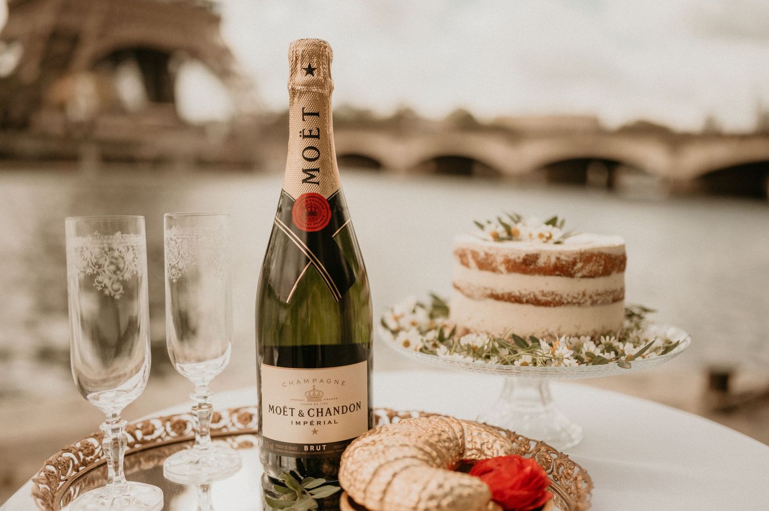 Moet champagne bottle and treats arranged on table with Eiffel Tower in background.