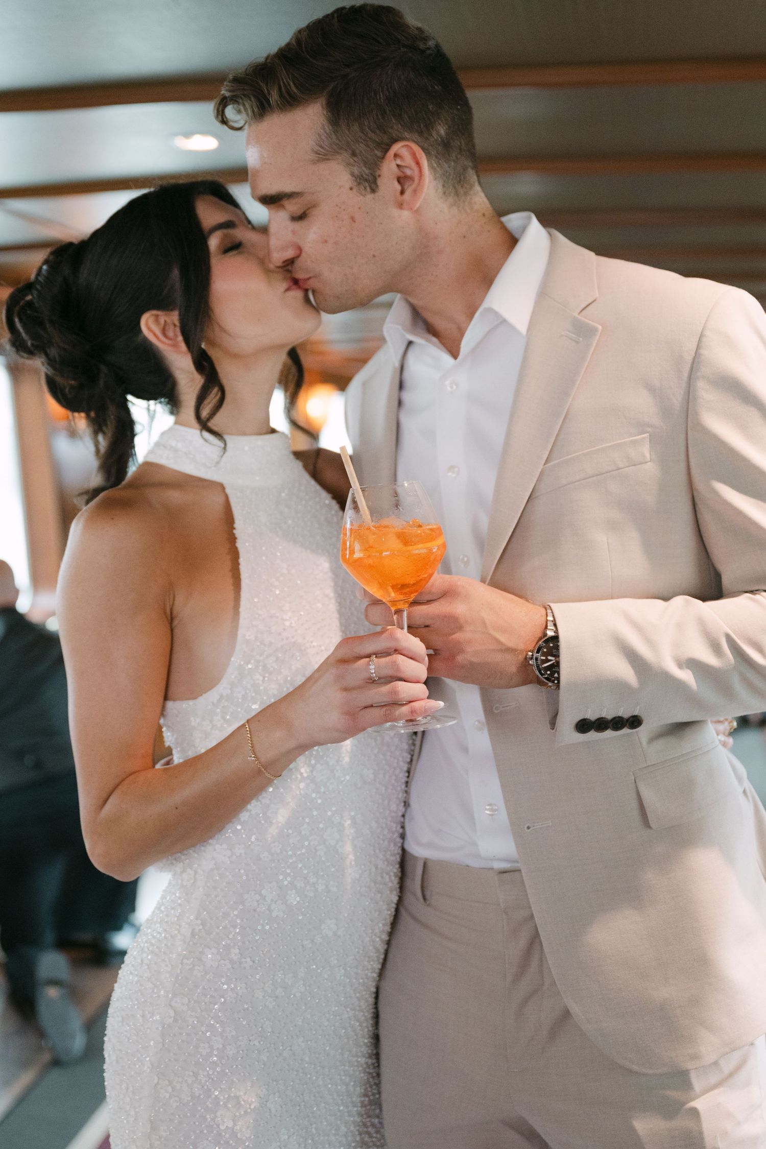 Romantic couple in wedding attire sharing intimate moments while holding orange cocktails at a reception.