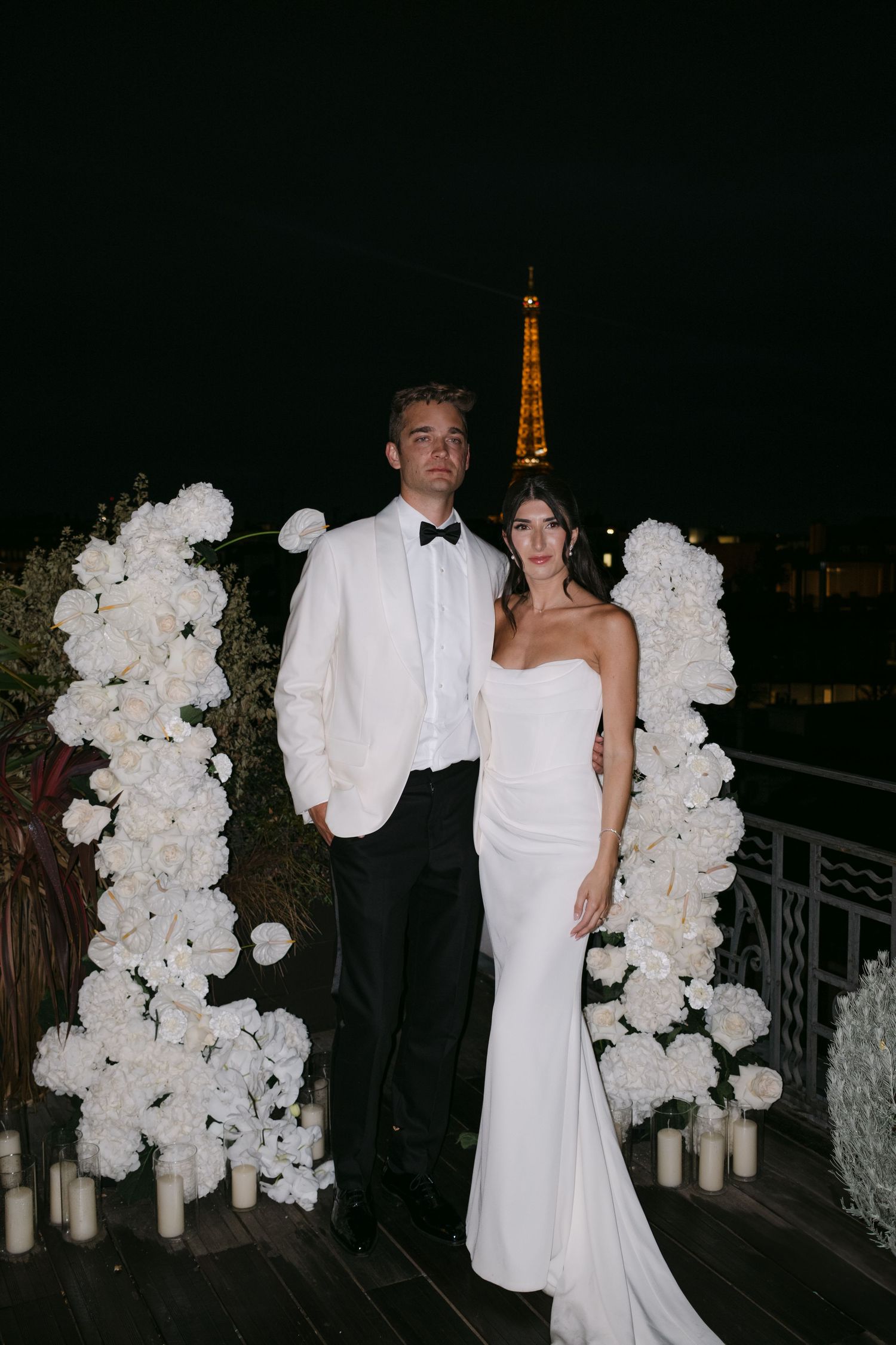 Bride and groom kissing in front of illuminated Eiffel Tower at night wedding.