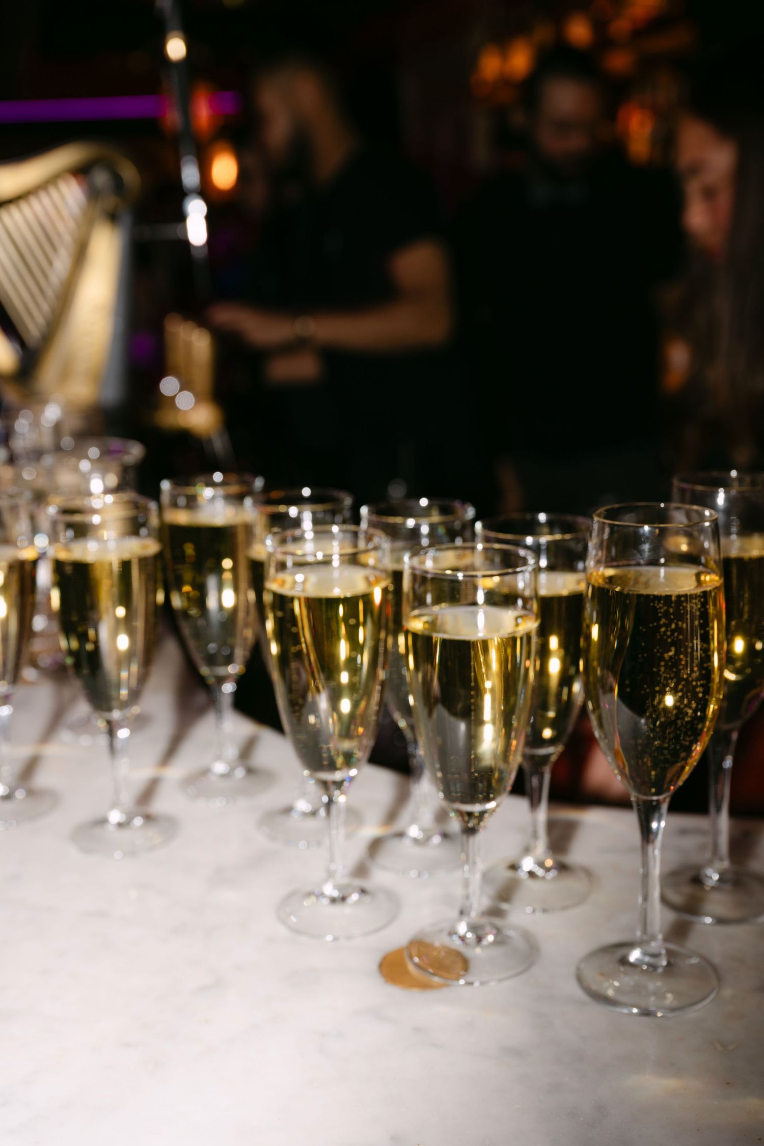 Rows of champagne flutes filled with sparkling wine lined up on a marble surface at an elegant party.
