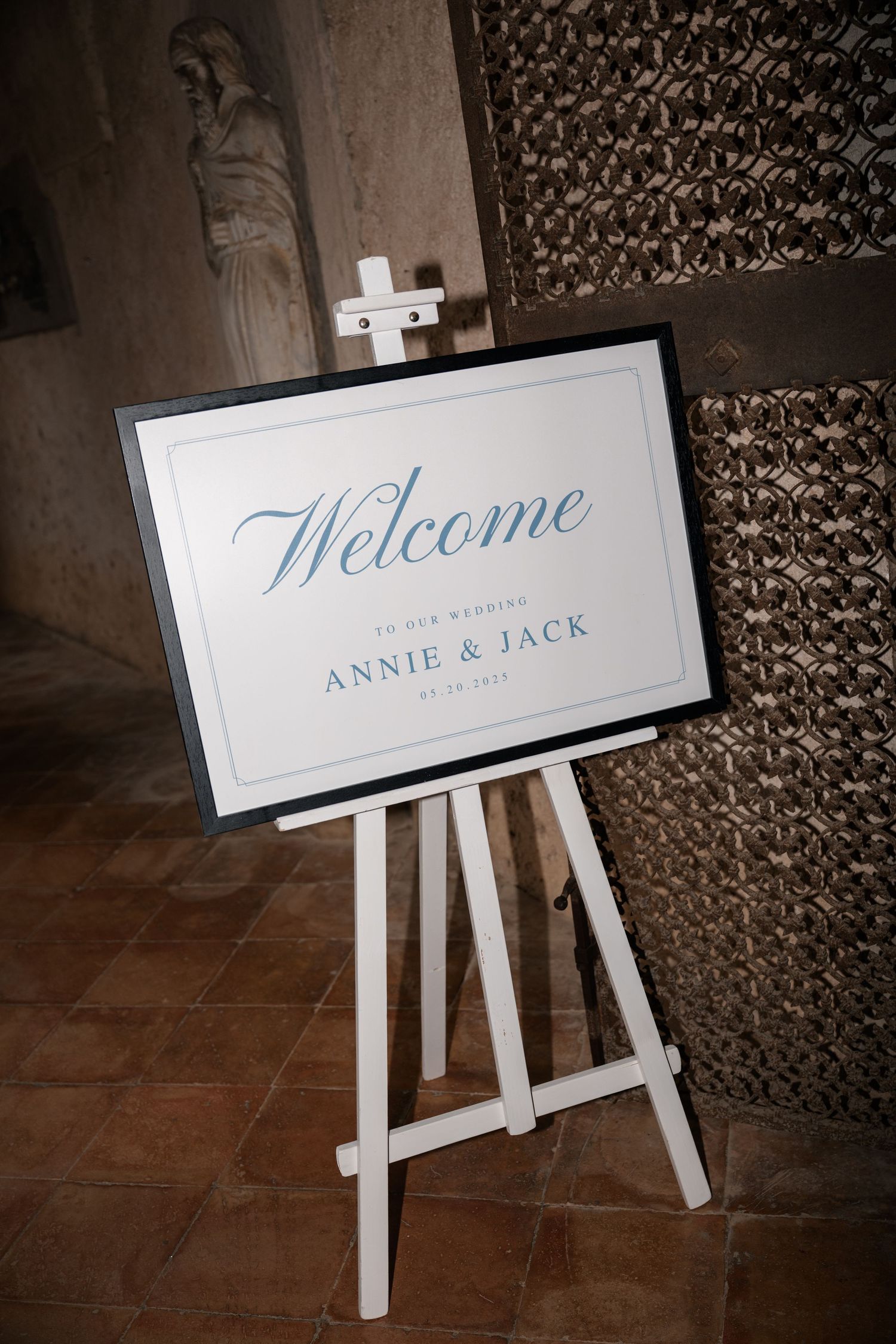 Elegant white wedding welcome sign for Annie and Jack displayed on wooden easel in stone venue.