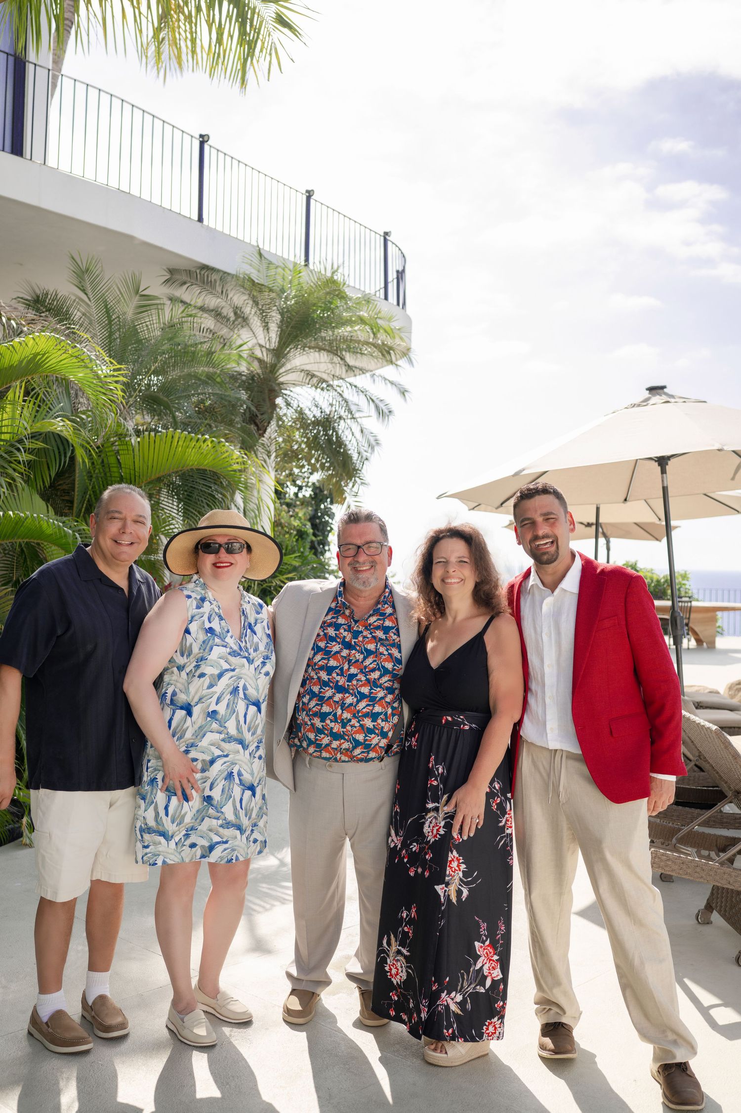 Five adults posing together outdoors at a tropical resort with palm trees and ocean views.