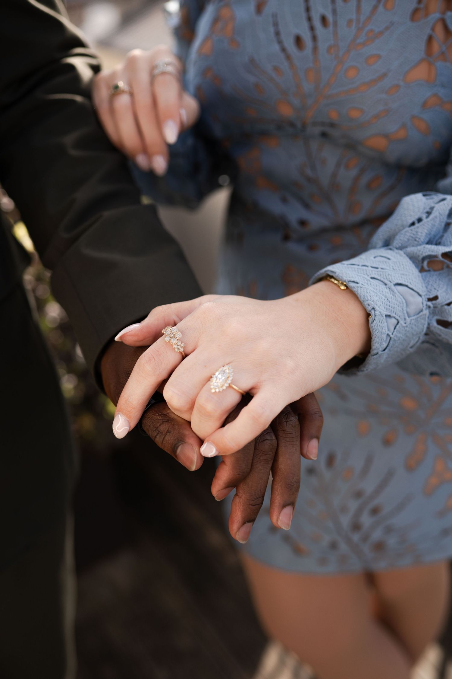 Close-up of an interracial couple holding hands, woman wearing a stunning marquise diamond engagement ring in rose gold.