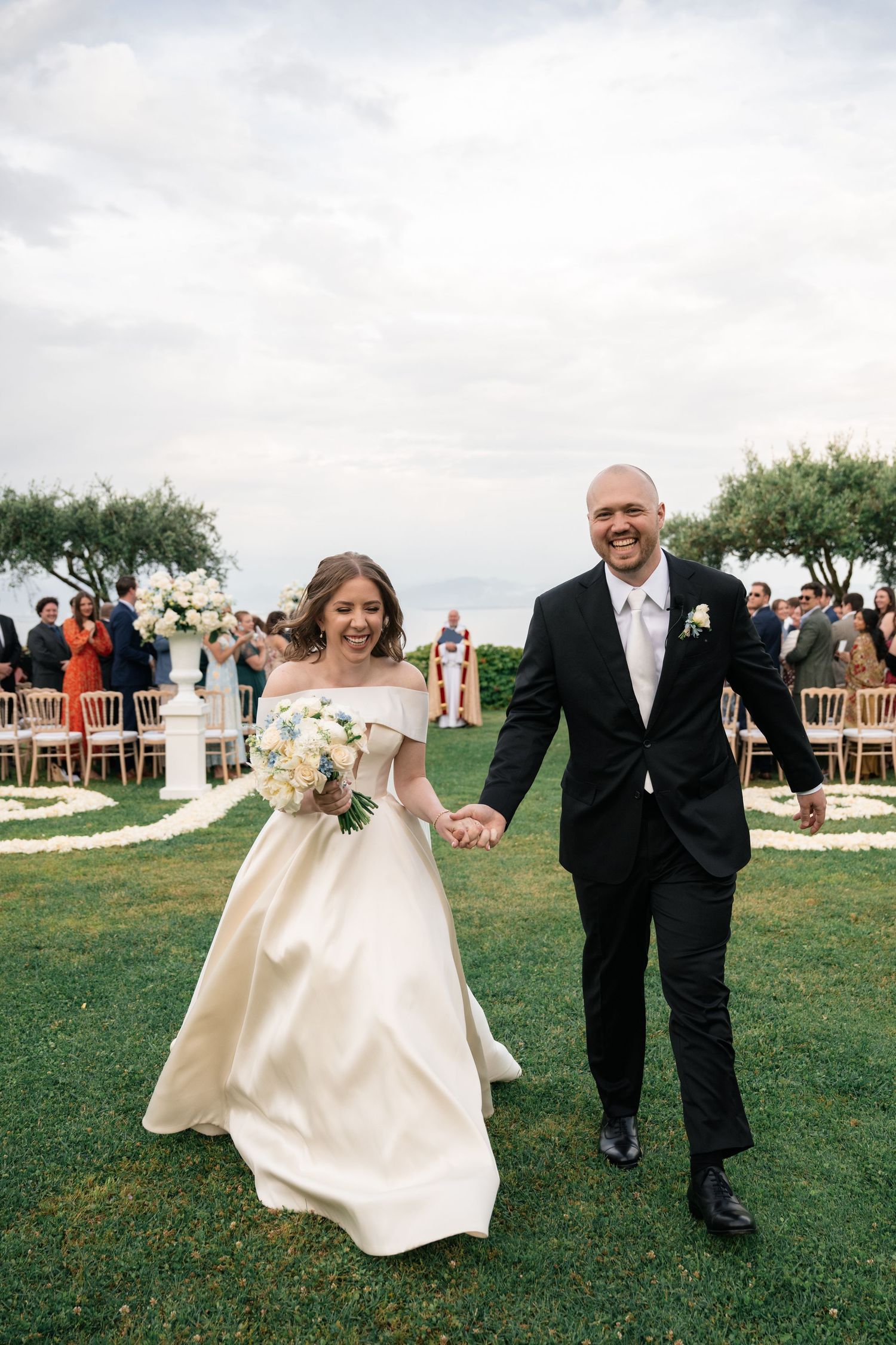 Joyful bride and groom walk hand in hand down aisle after outdoor wedding ceremony by the sea.