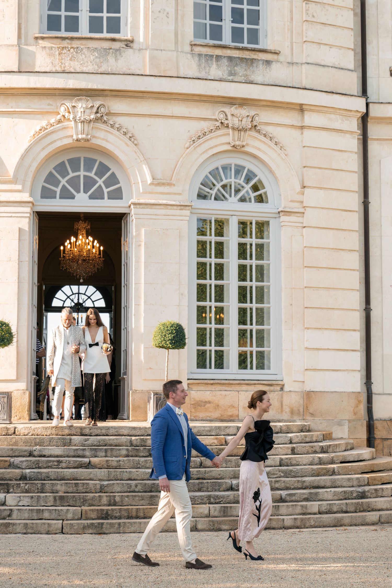 Couple holding hands walking down stone steps of a grand French chateau wedding venue.