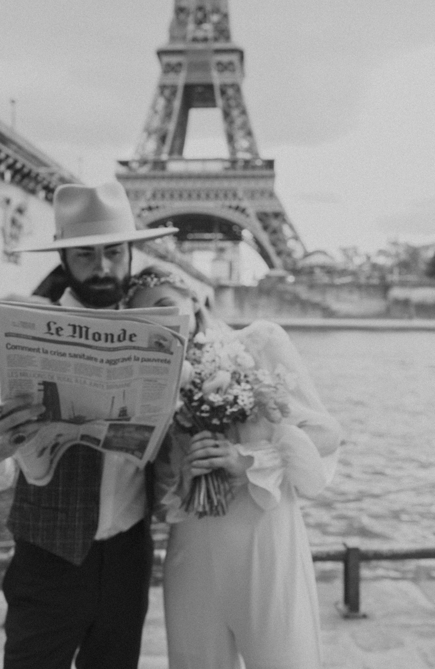 A black and white photo of a couple posing with Le Monde newspaper near the Eiffel Tower.