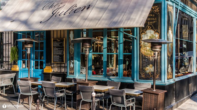 Charming Parisian cafe with blue-framed windows and outdoor bistro seating under an awning.