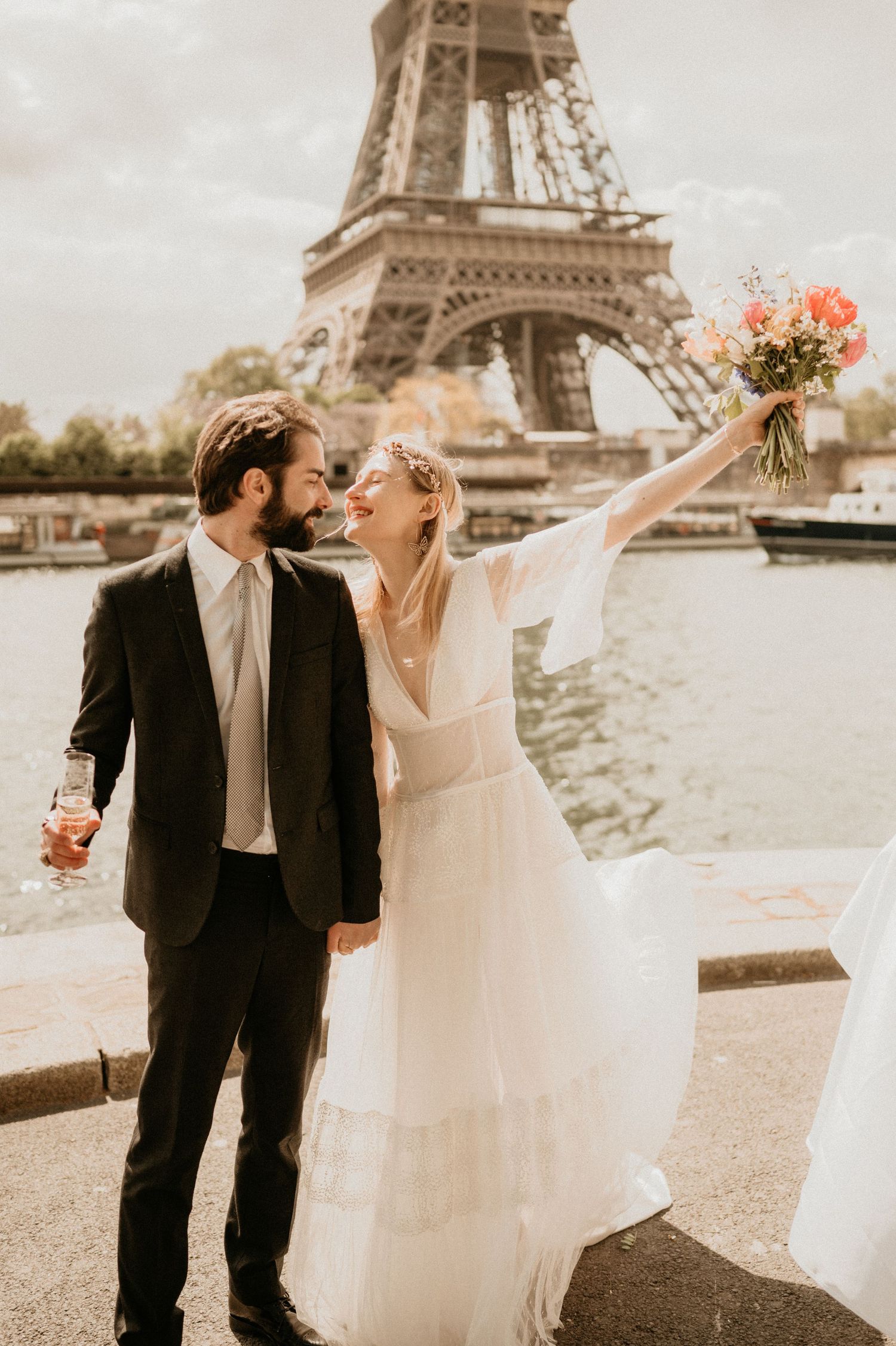 Joyful bride raises bouquet while celebrating with groom near Eiffel Tower.