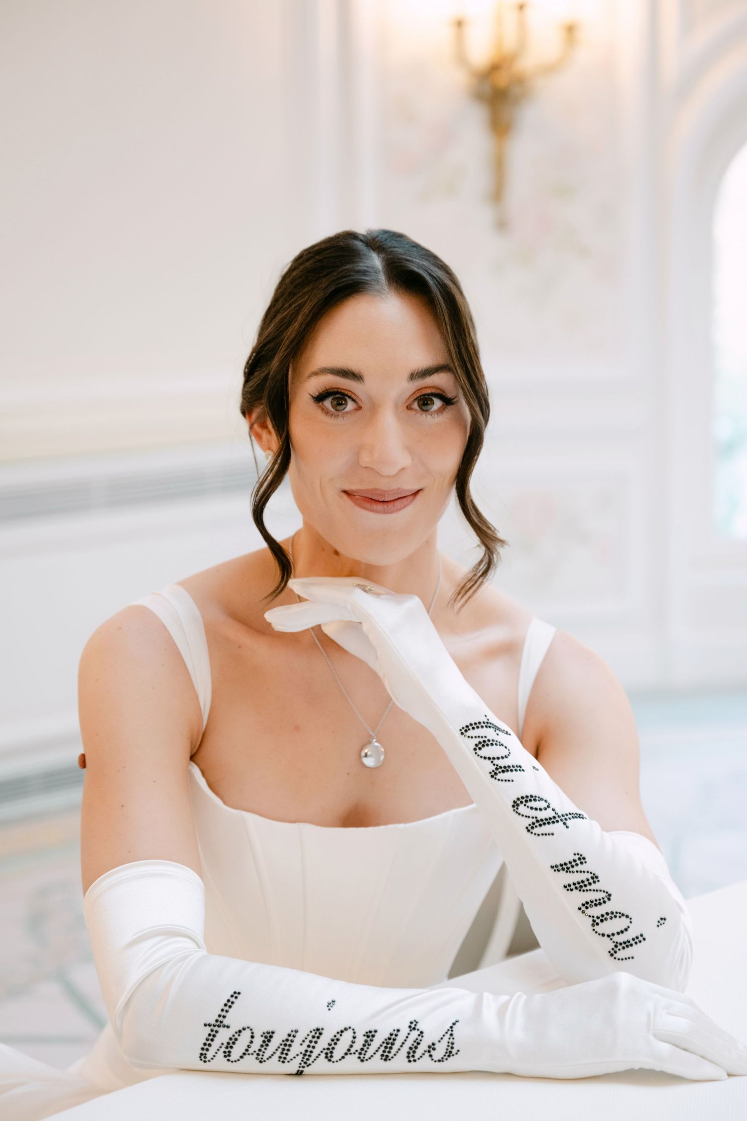 Bride in white gown wearing long satin gloves with toi et moi toujours rhinestone text posing elegantly.