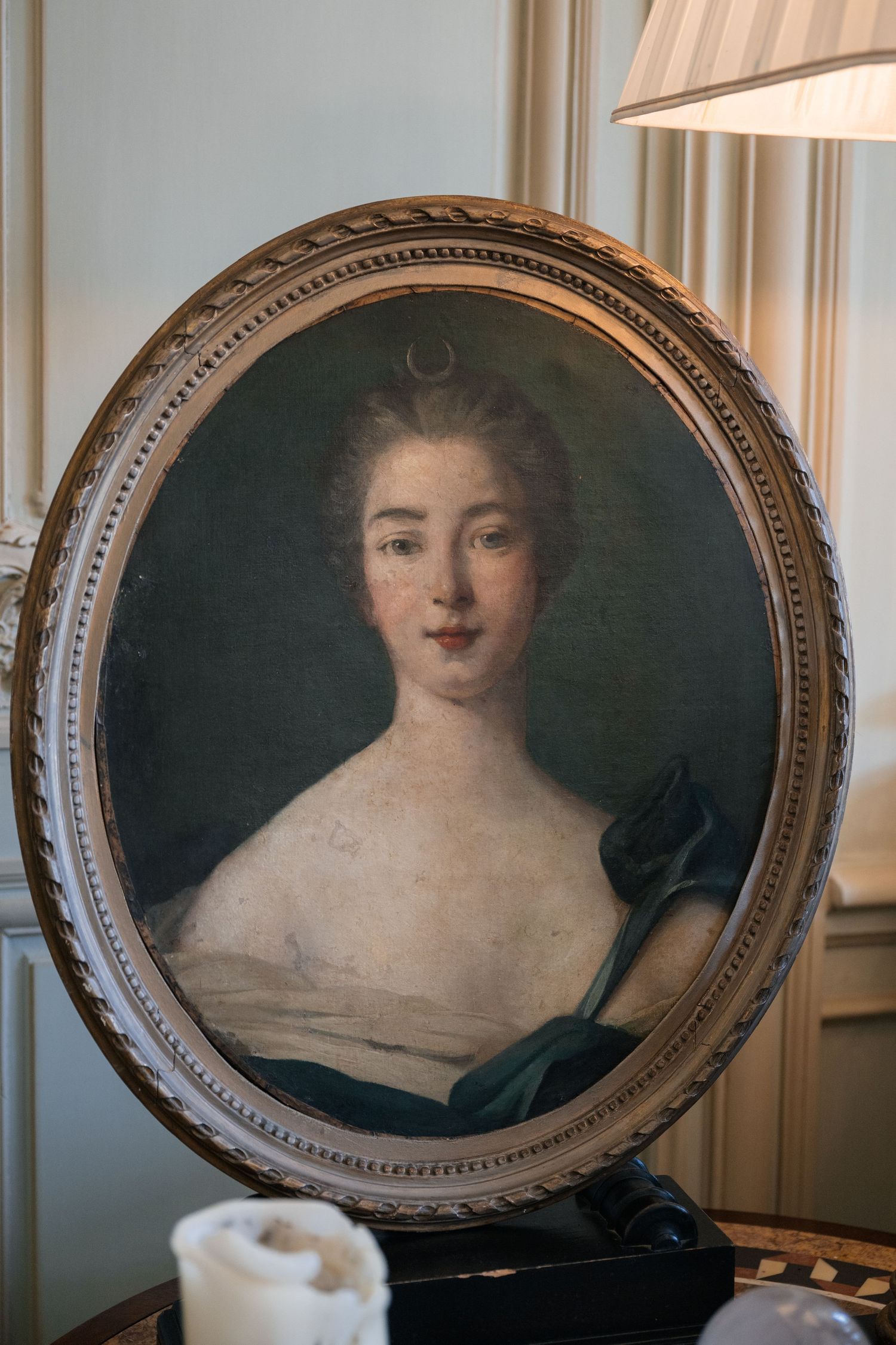 Antique oval-framed oil portrait painting of an elegant woman in classical style displayed on a table.