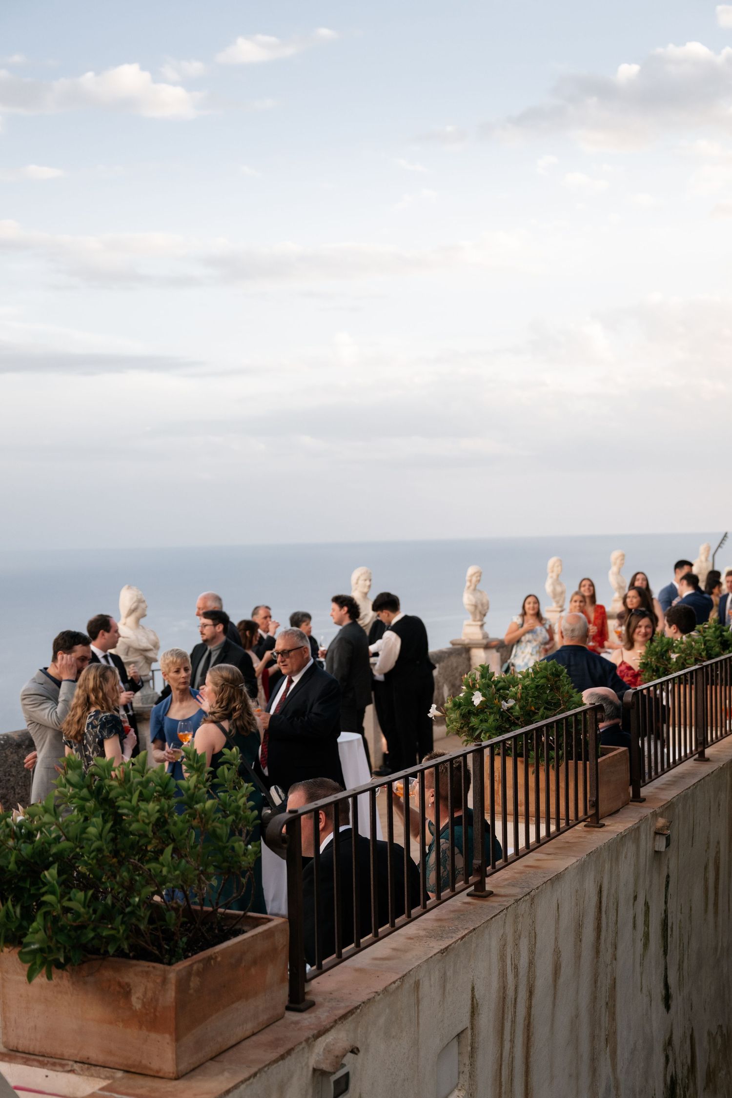 Wedding guests mingle on terrace overlooking stunning Mediterranean Sea at Villa Cimbrone in Ravello Italy.