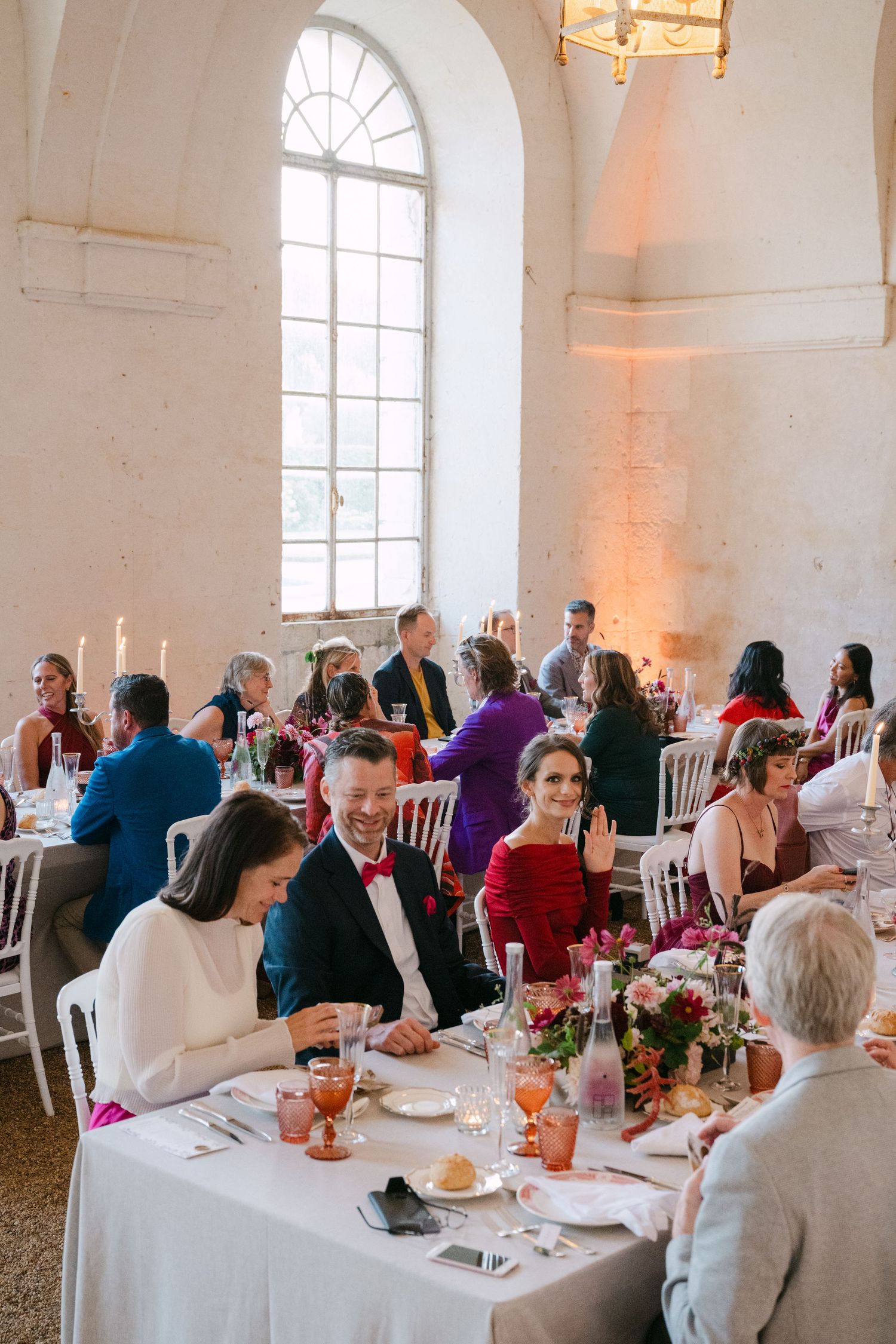 Wedding reception guests seated at decorated tables in a bright stone venue.