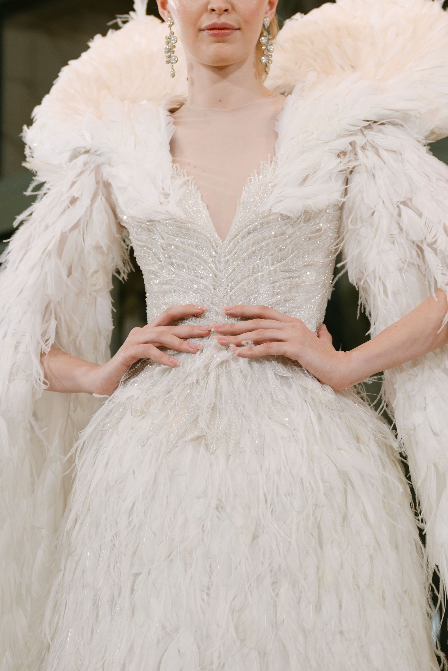 Luxurious white feathered wedding gown with beaded bodice and dramatic feather sleeves on runway.
