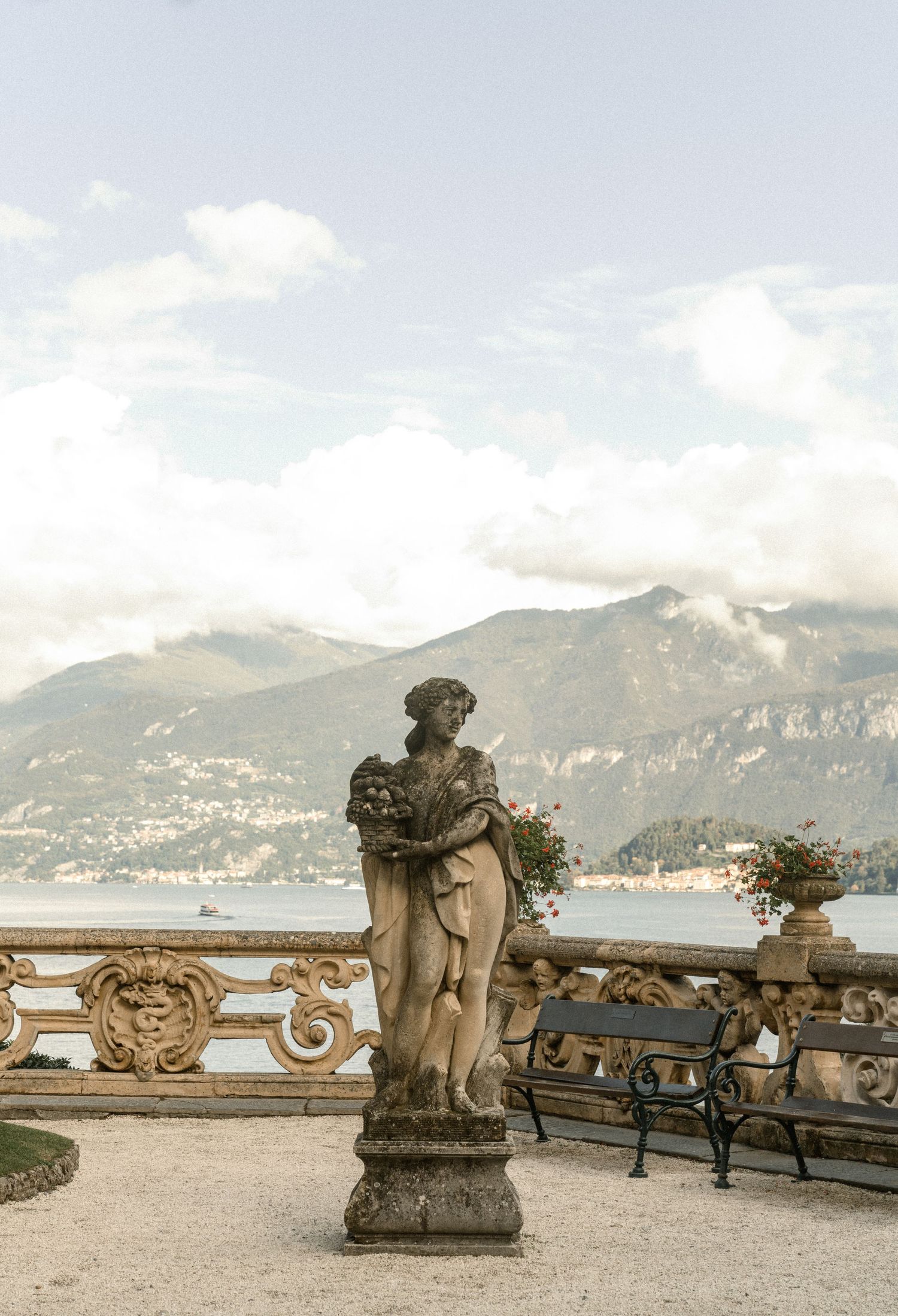 Classical stone statue on ornate balustrade overlooking Lake Como with mountains in background.