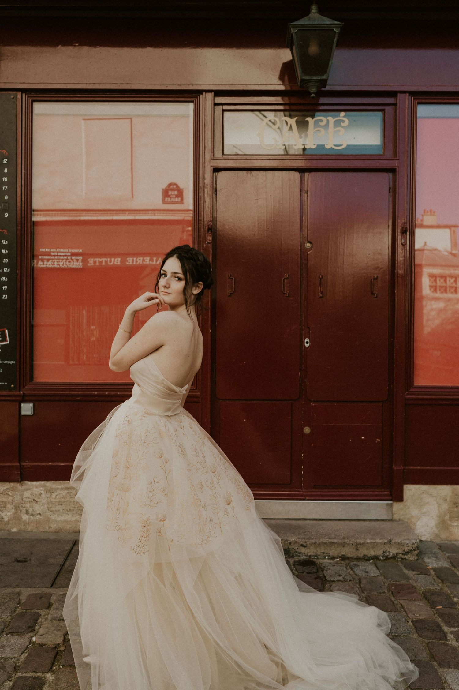 Warm-toned wedding photo capturing elegant pose against vintage Parisian restaurant exterior.
