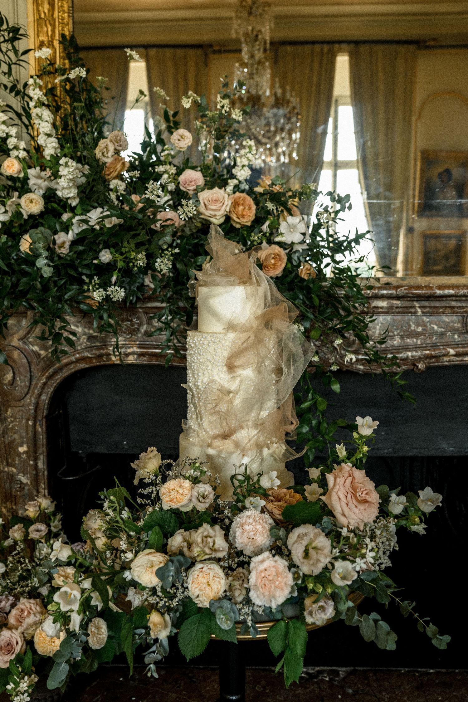 Luxurious floral arrangement with blush roses cascades over an antique fireplace mantel.