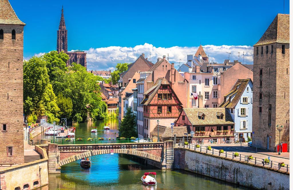Historic medieval buildings and bridges along a canal in Strasbourg, France with cathedral spire in background.