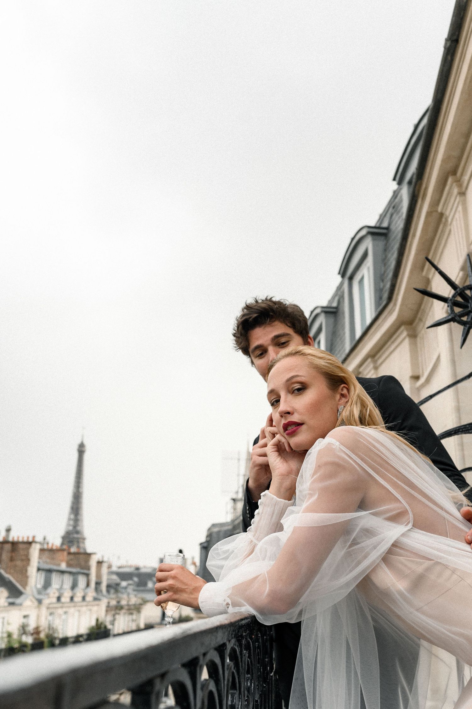 Couple in wedding attire on a Parisian balcony with the Eiffel Tower in the background.