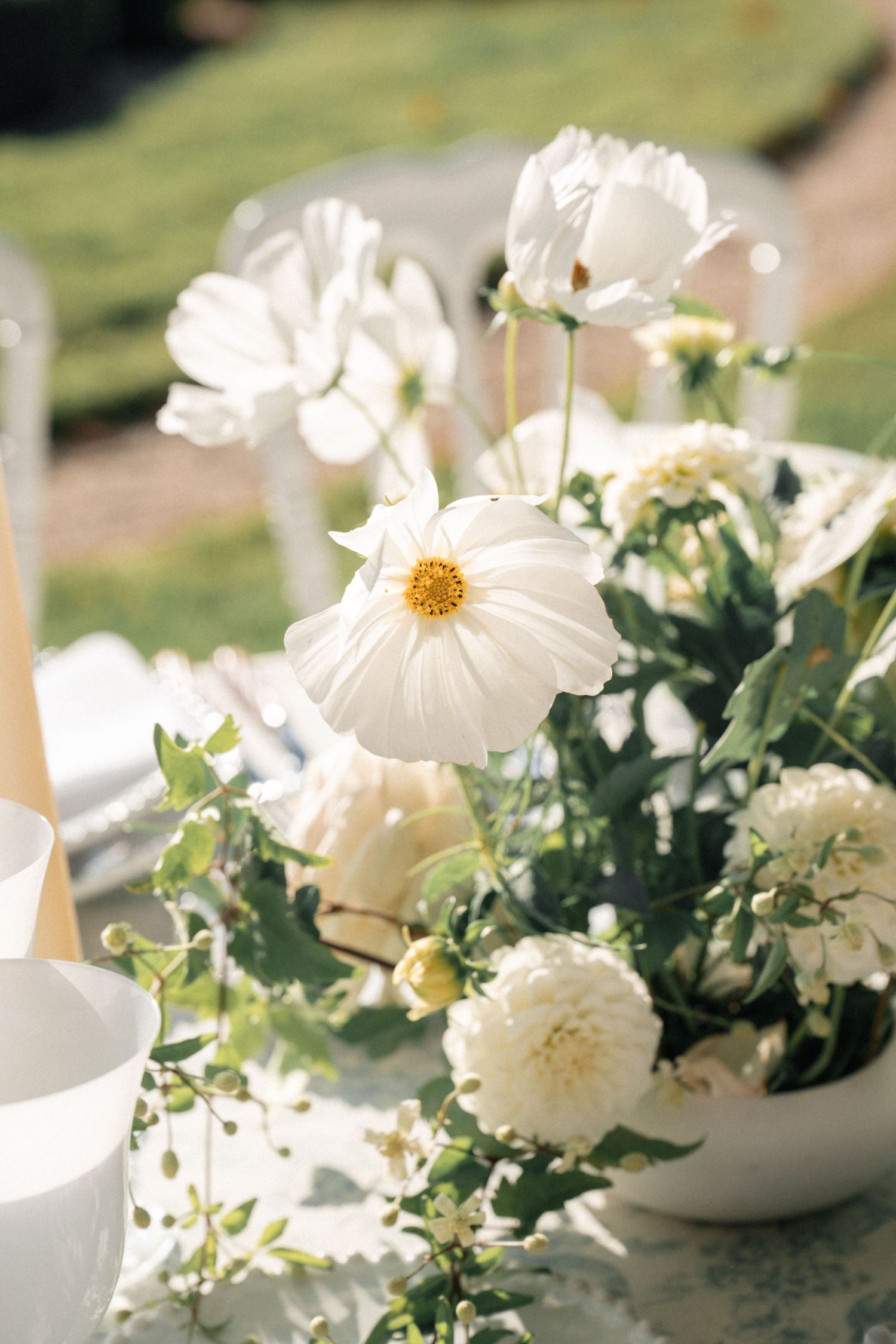 White cosmos and dahlia flowers in a ceramic bowl centerpiece on an elegant outdoor dining table.